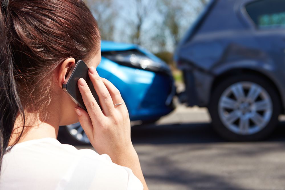 A Woman Is Talking On A Cell Phone In Front Of A Car Accident — Spray Tech Smash Repairs In Gympie, QLD