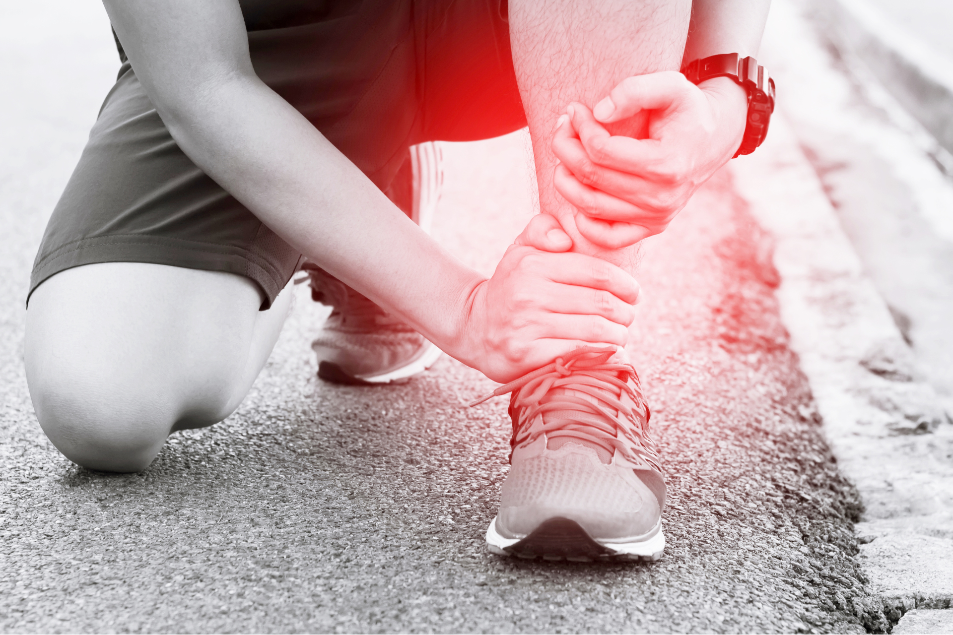 A person is kneeling down and holding their ankle in pain.