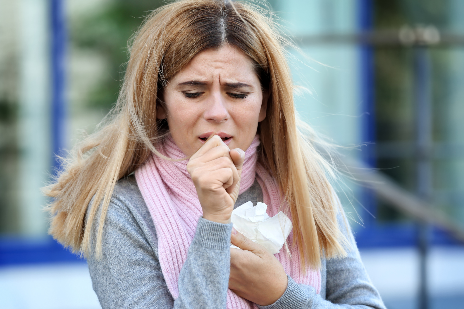 A woman is coughing into a napkin while wearing a scarf.