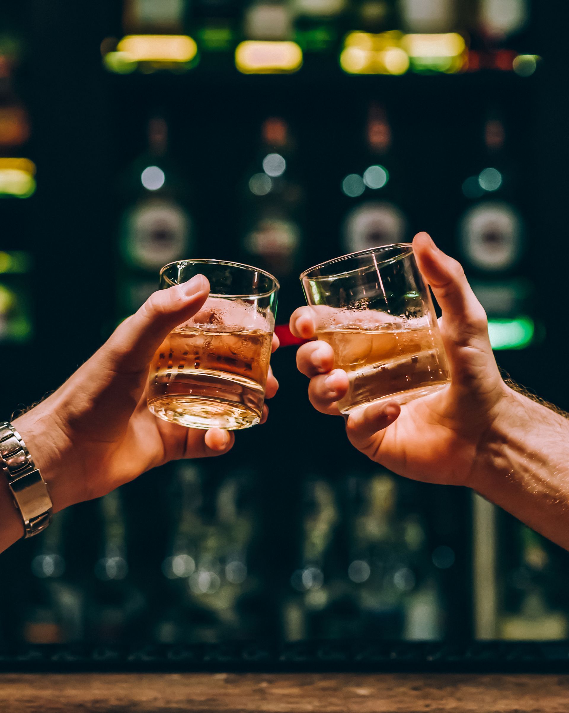 Bartender pouring a red cocktail beside two garnished drinks on a bar counter.