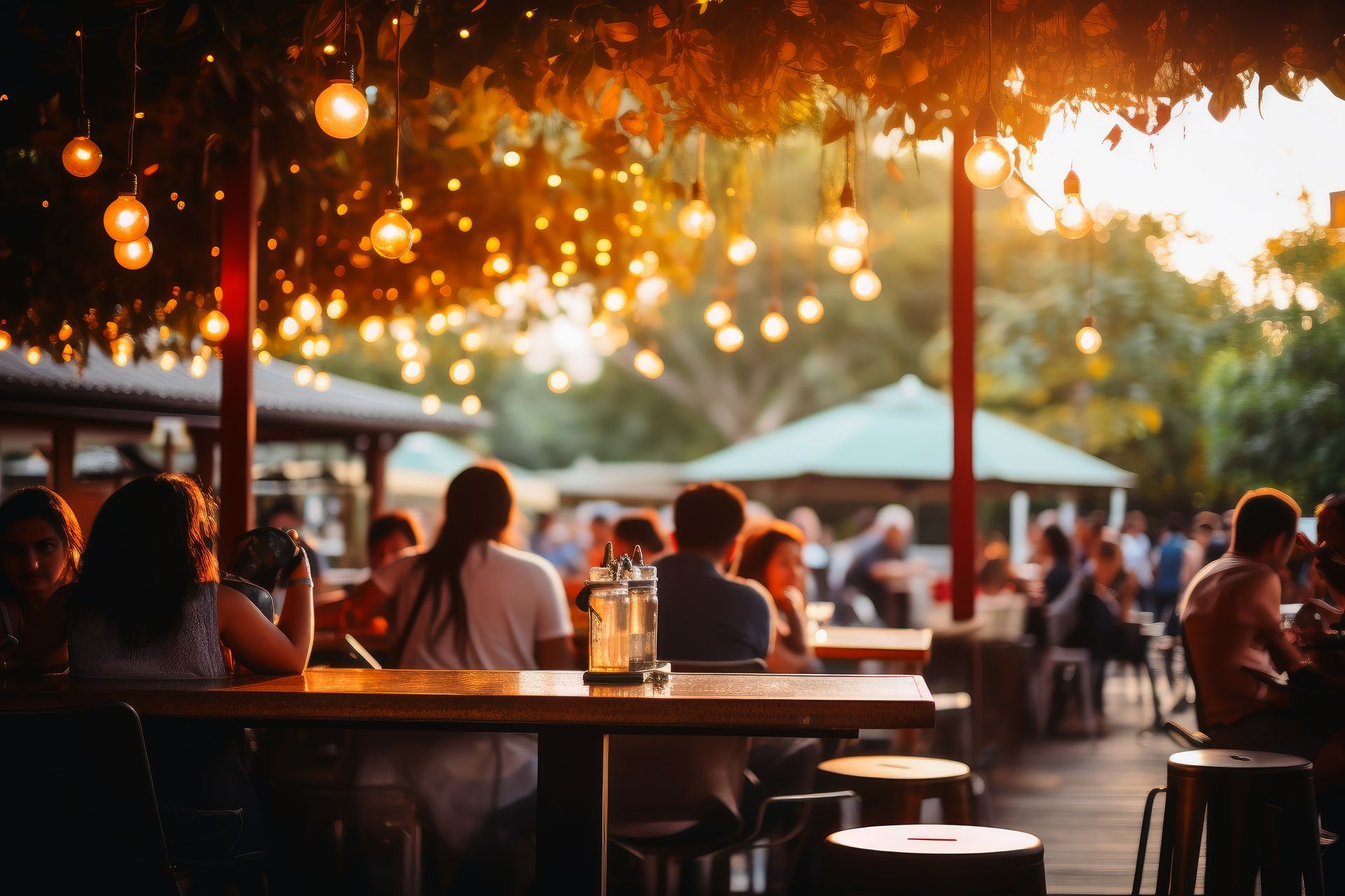 Outdoor café at sunset with hanging string lights, seated diners, and warm golden glow