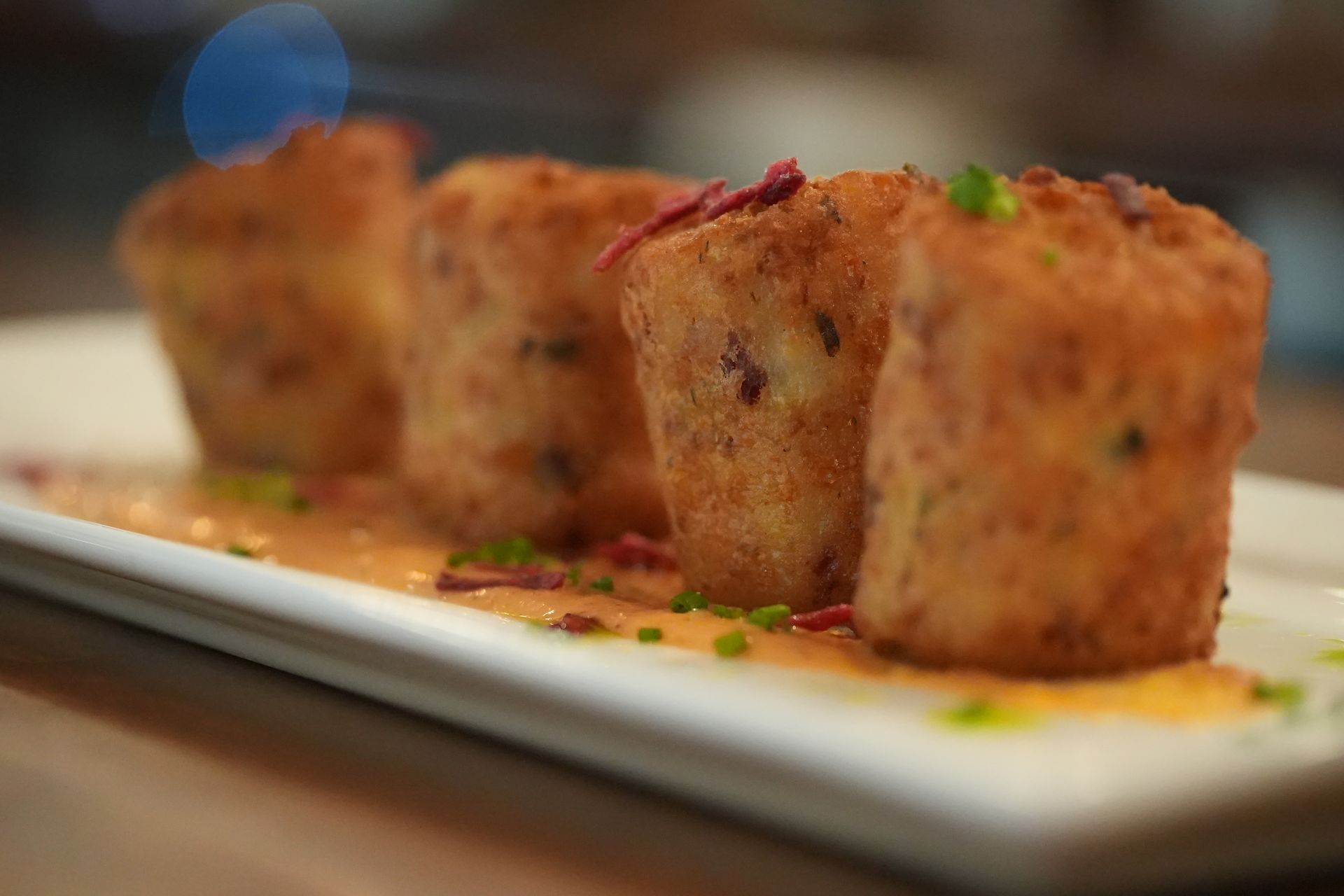 Plated golden-brown appetizers drizzled with sauce and garnished with herbs on a white rectangular dish