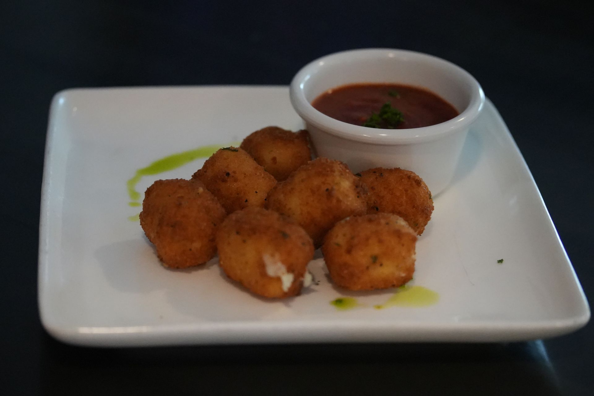 Plate of golden fried bites with a small bowl of dipping sauce on a white platter