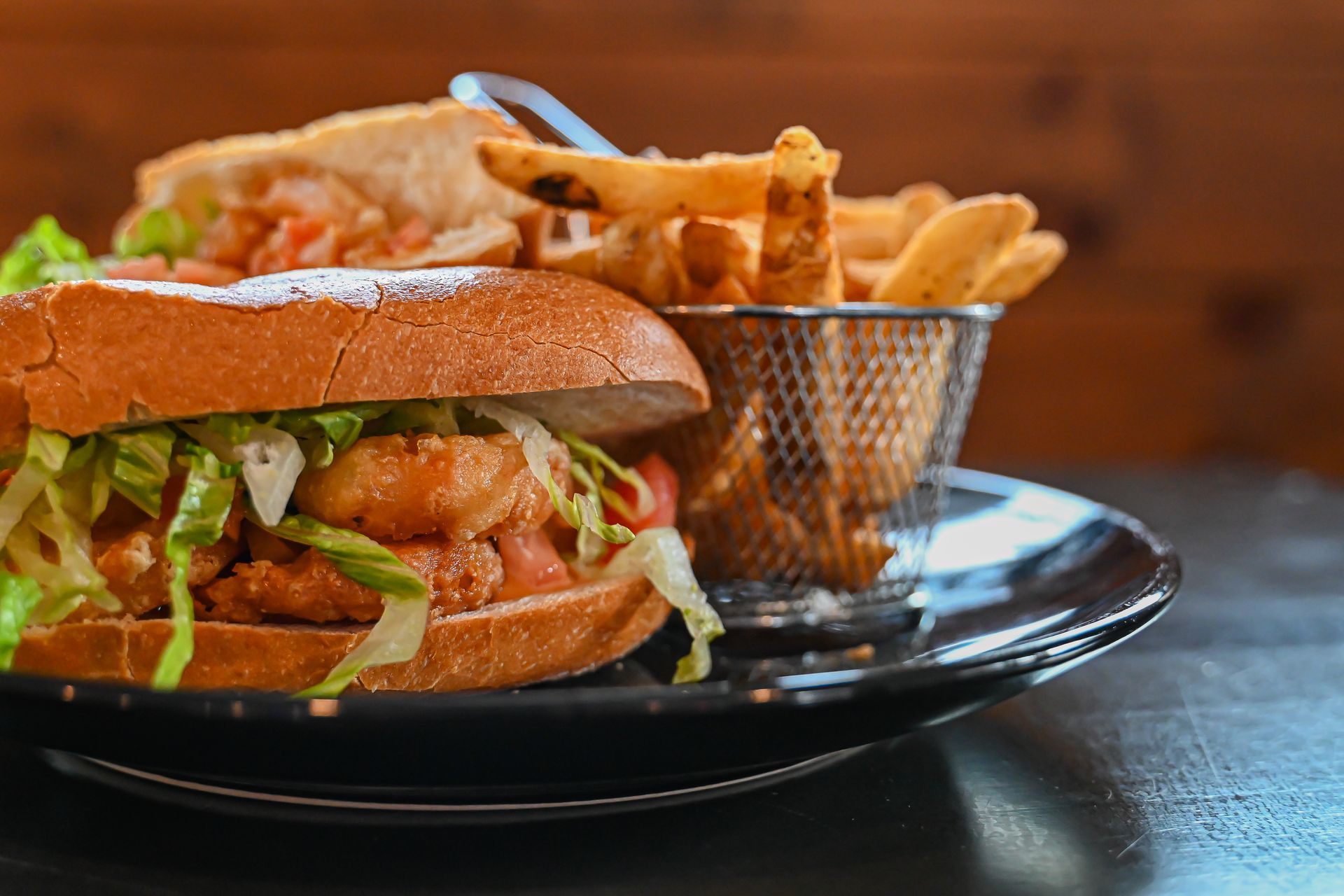 Sandwich and fries on a black plate with a metal basket, on a wooden table