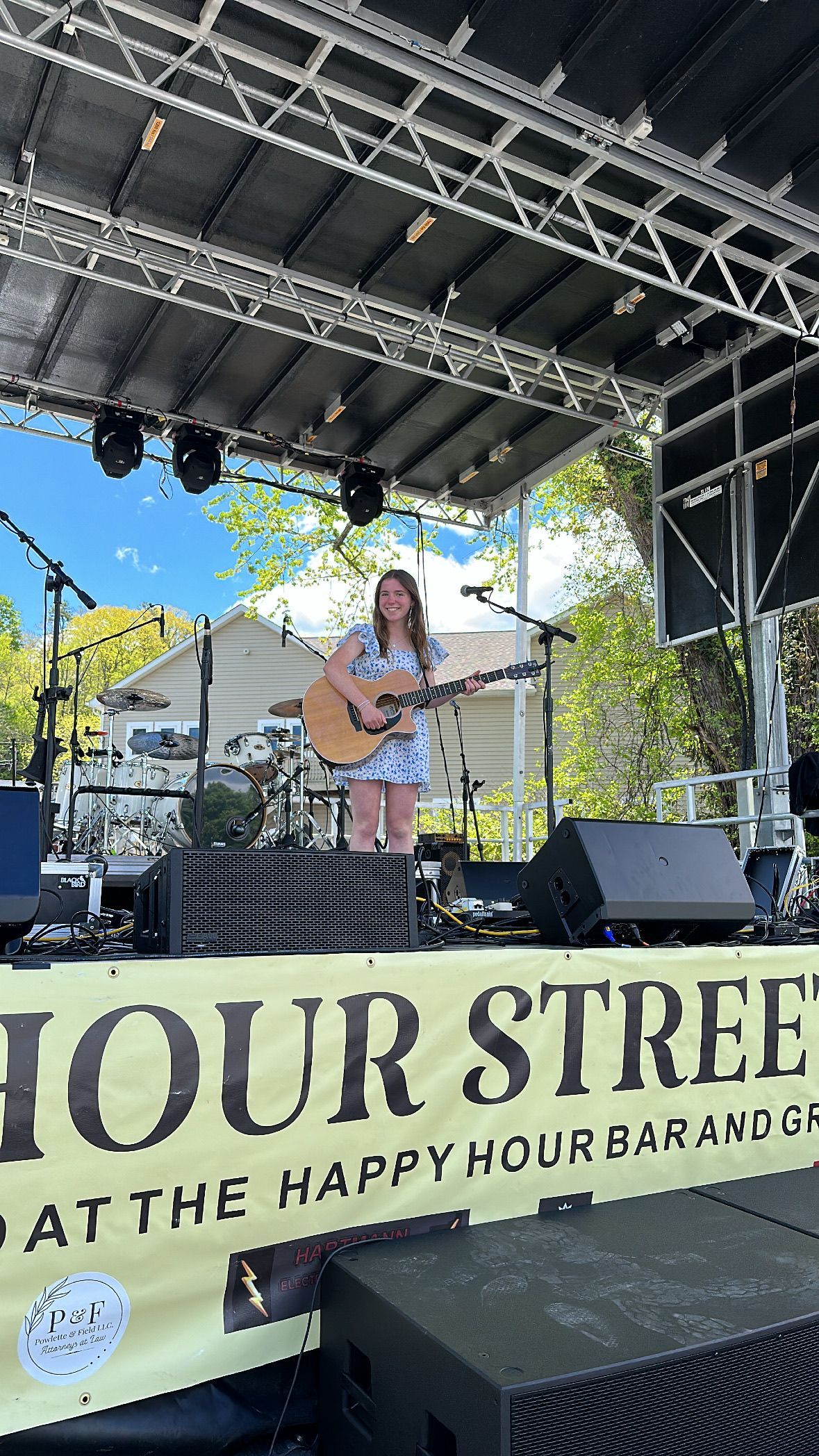 A woman is playing a guitar on a stage at Happy Hour Street Fest