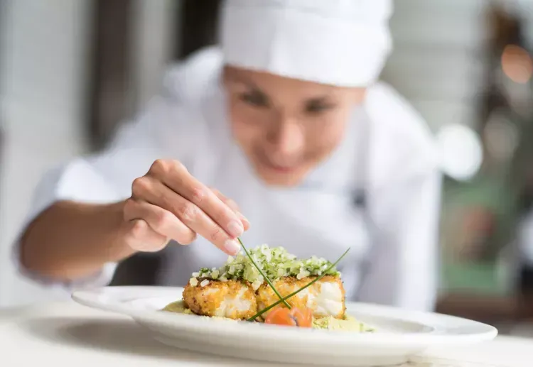 A chef is decorating a plate of food with greens. A chef is decorating a plate of food with greens.