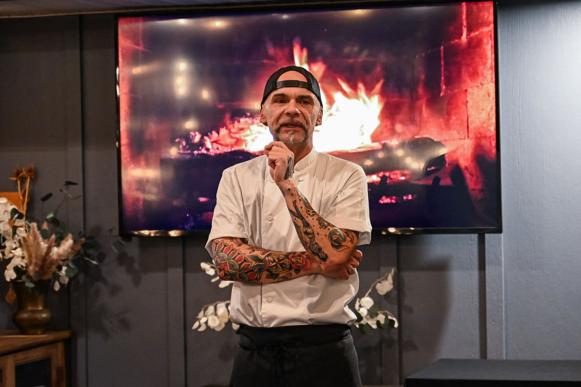 A man with tattoos is standing in front of a television.