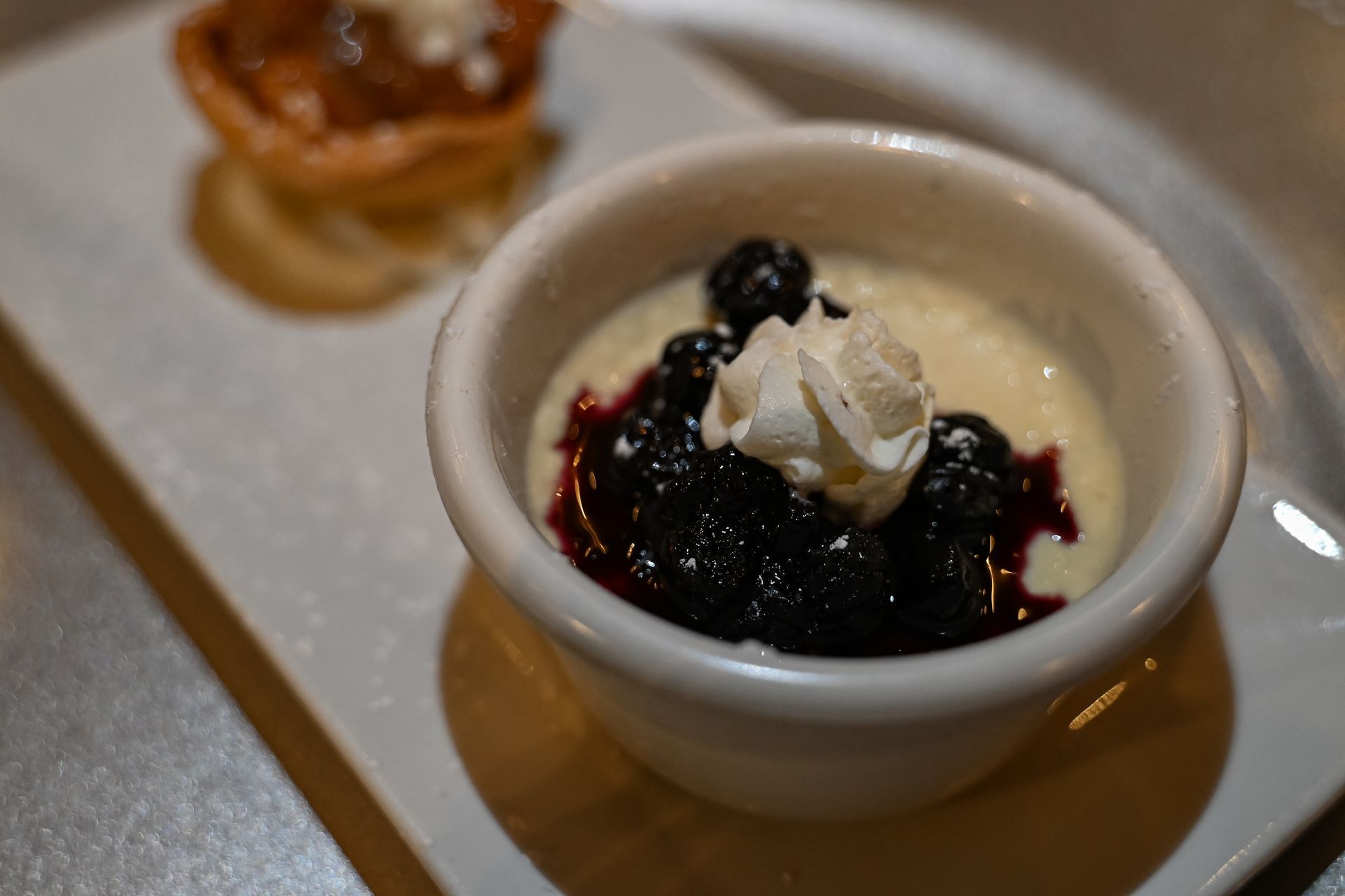 A bowl of dessert with whipped cream and blueberries on a plate.