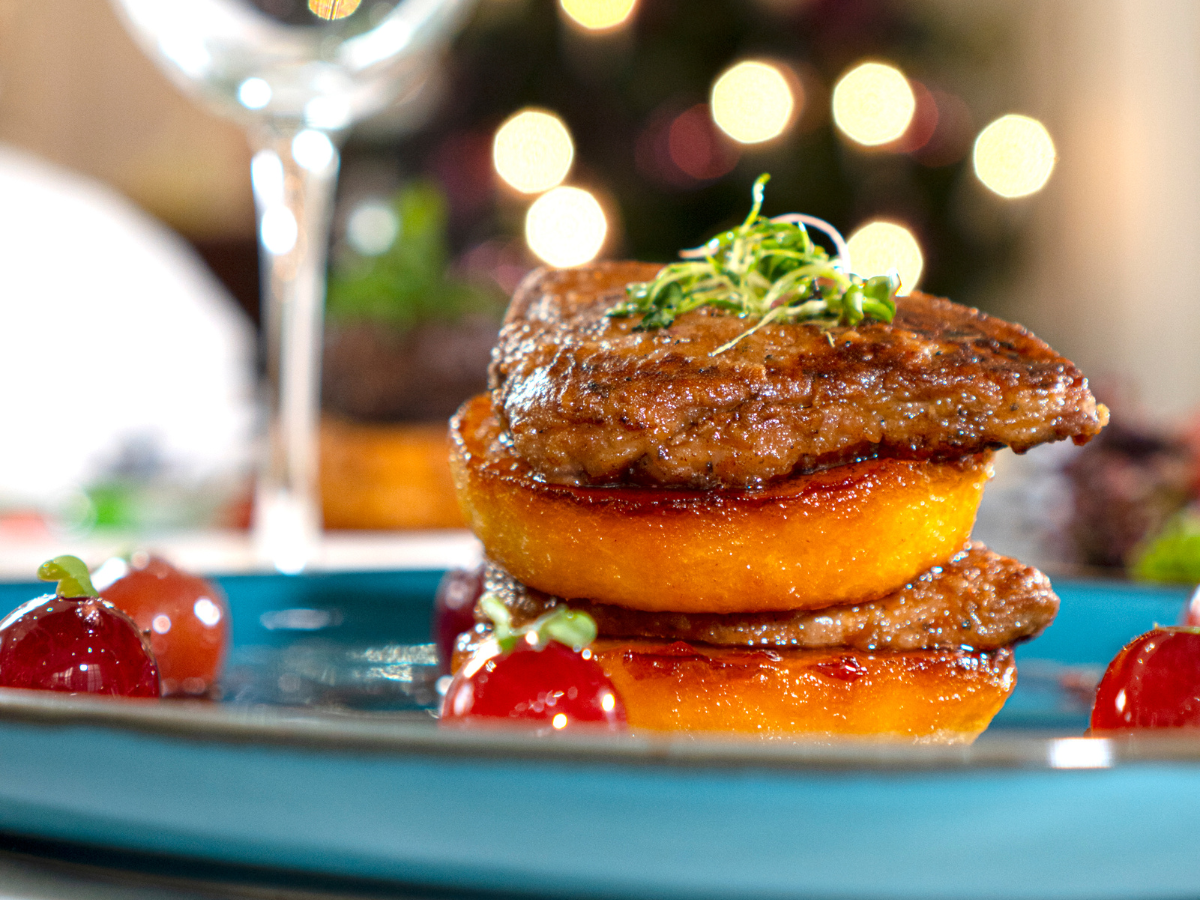 A close up of a plate of food with a glass of wine in the background.