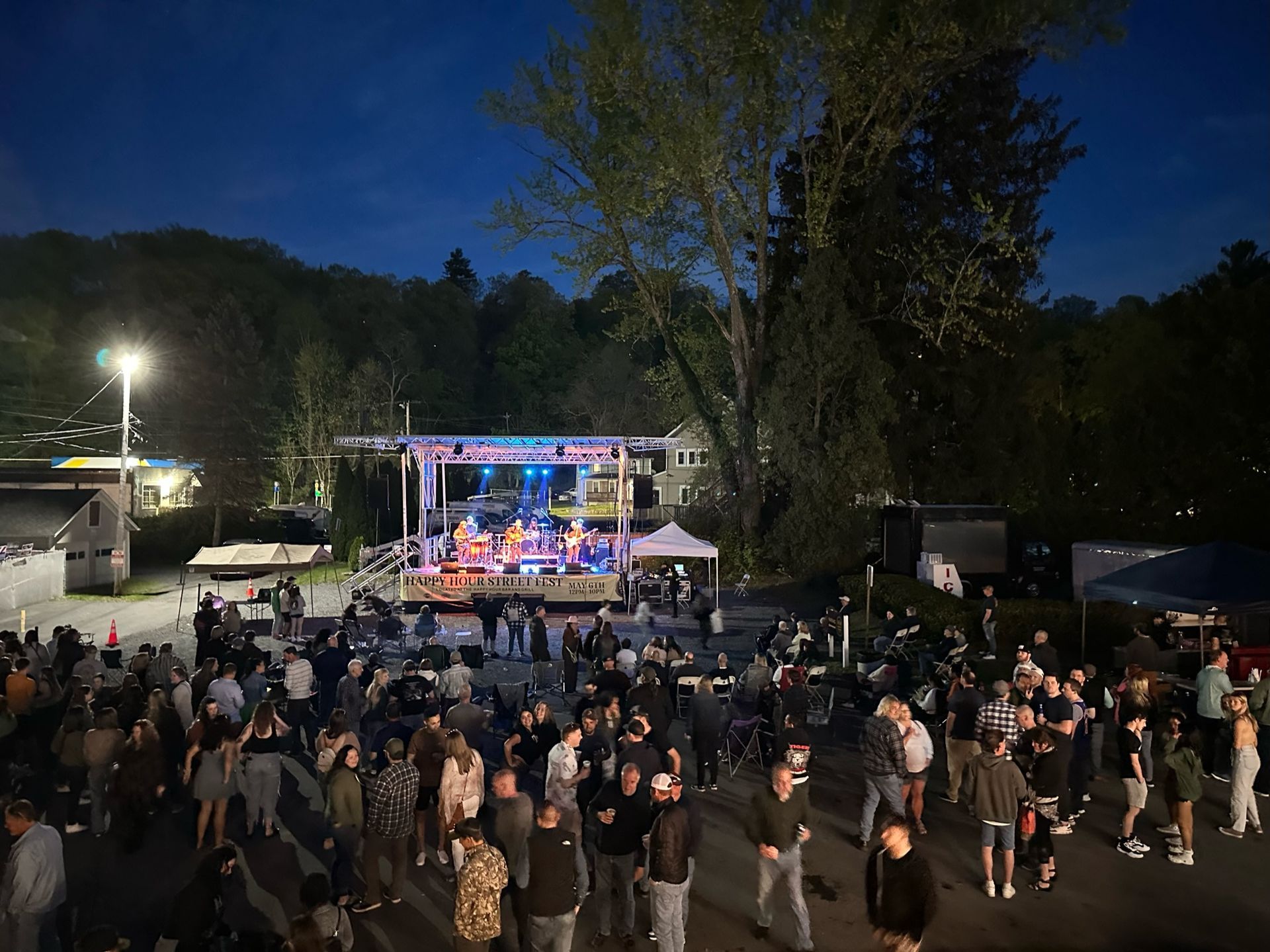 A large group of people are standing in front of a stage at a concert at Happy Hour Street Fest