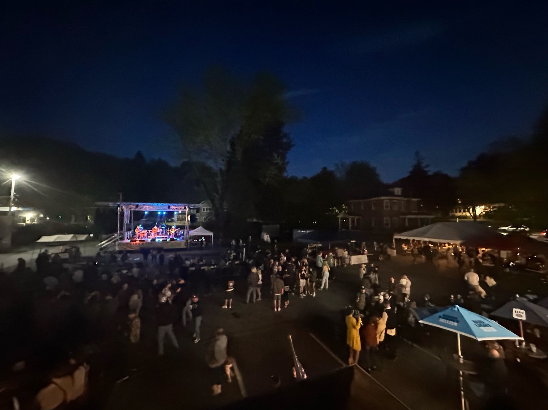 A group of people are standing in front of a stage at night for Happy Hour Bar & Grill Street Fest