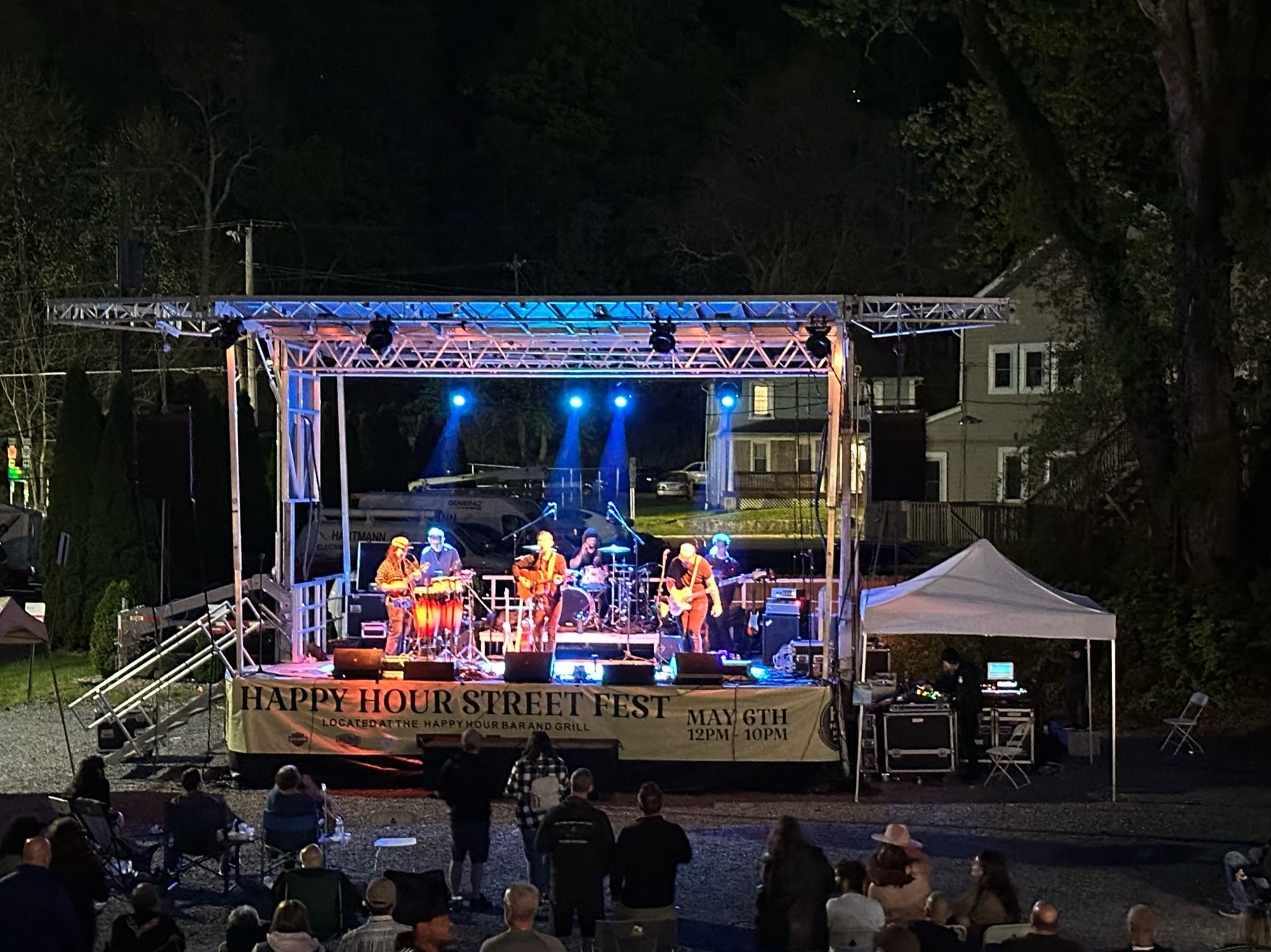 A group of people are standing in front of a stage at night at Happy Hour Street Fest