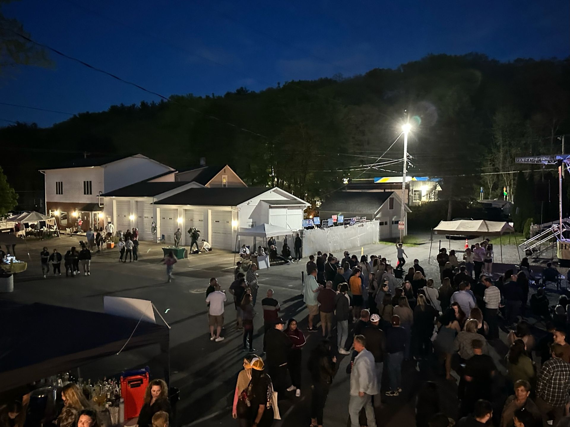 A large group of people are gathered in a parking lot at night for Happy Hour Street Fest