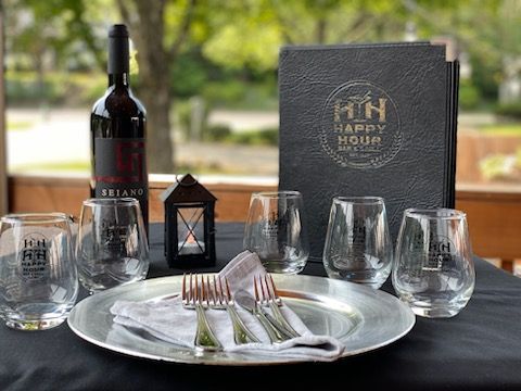 Elegant wine and dinner place setting with glasses, silverware, bottle, lantern, and menu on a black tablecloth