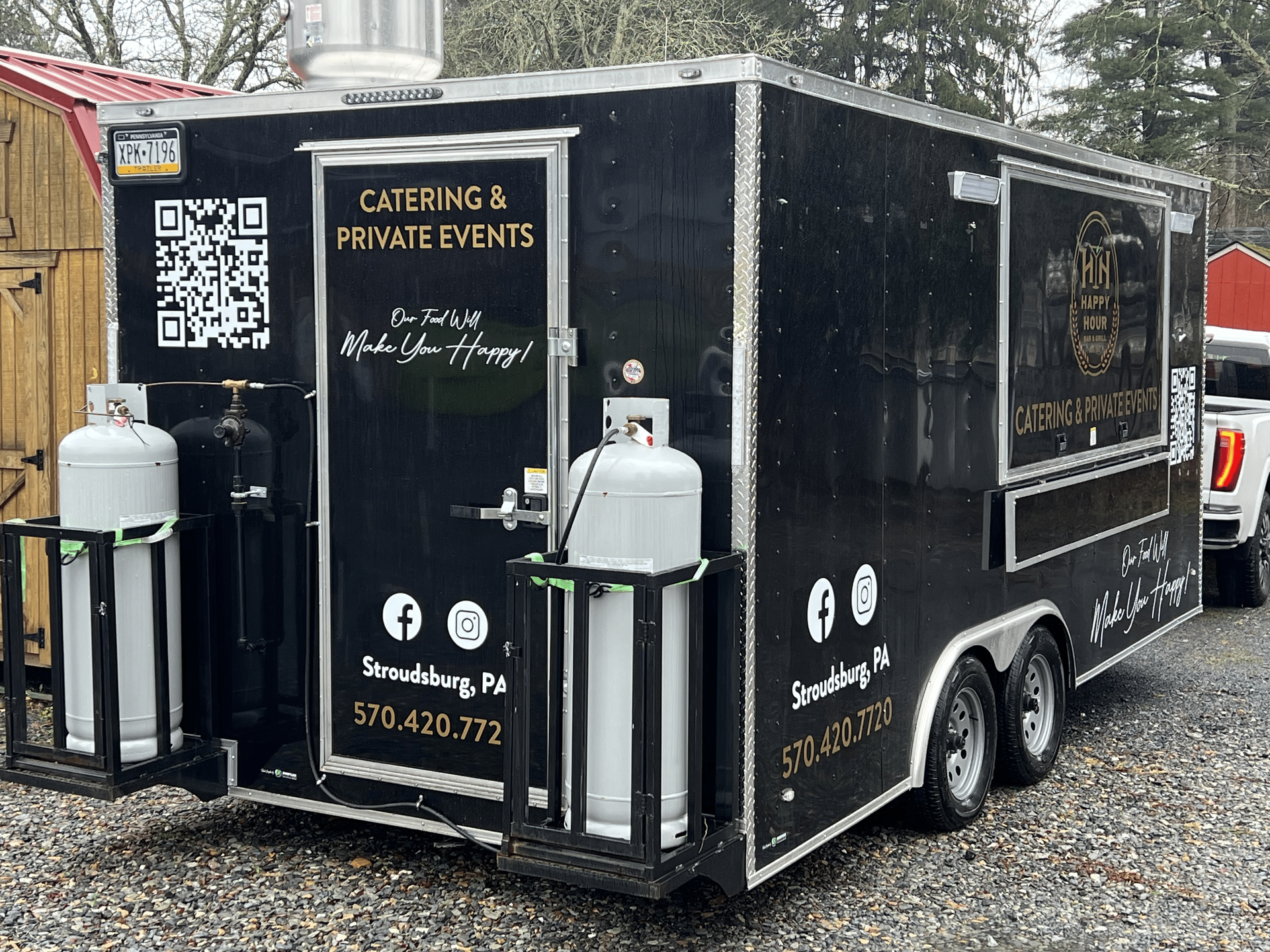 Happy Hour Bar & Grill black food truck is parked in a gravel lot next to a truck.