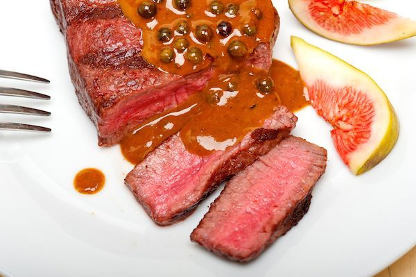 A white plate topped with meat and sauce with a fork A white plate topped with meat and sauce with a fork
