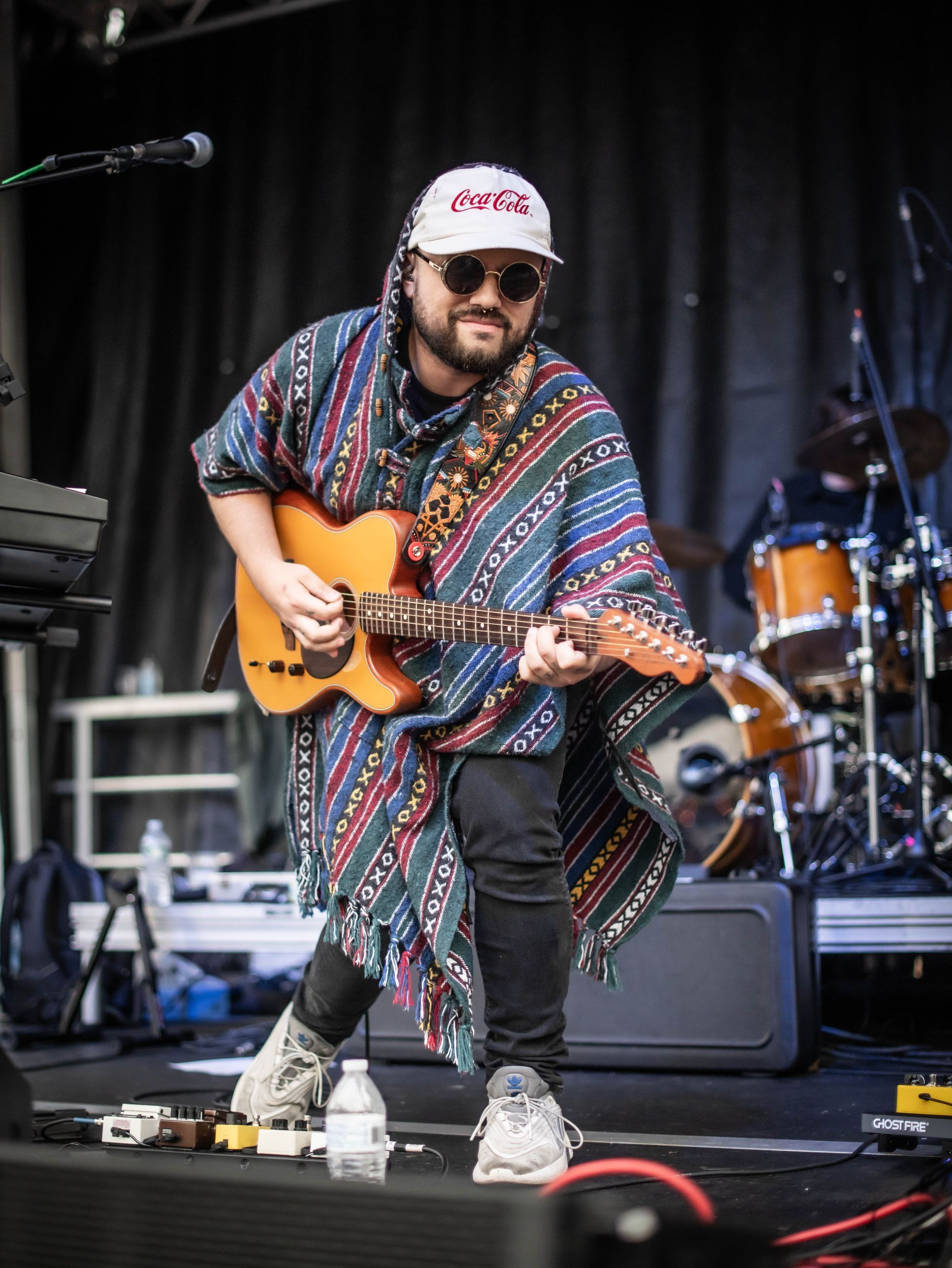 Musician in patterned poncho and cap playing electric guitar onstage during a live performance