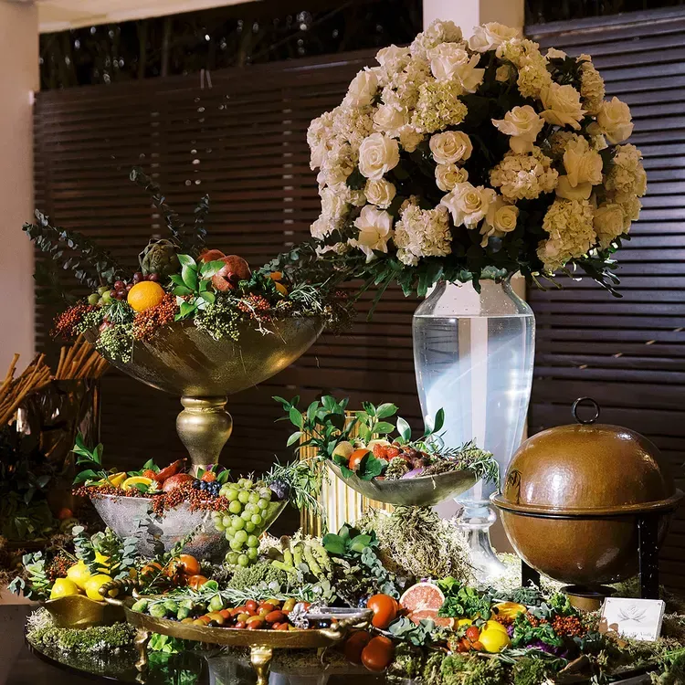 A table topped with bowls of fruit and flowers at a wedding. A table topped with bowls of fruit and flowers at a wedding.