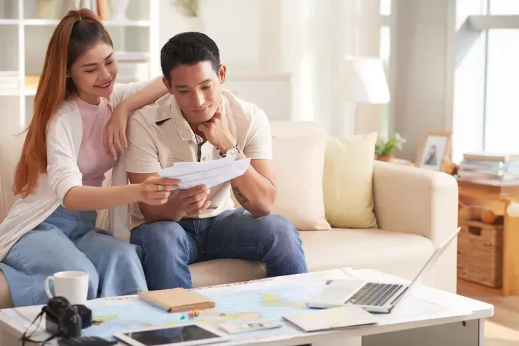 A man and a woman are sitting on a couch discussing what caterer they want to pick for their wedding. A man and a woman are sitting on a couch discussing what caterer they want to pick for their wedding.