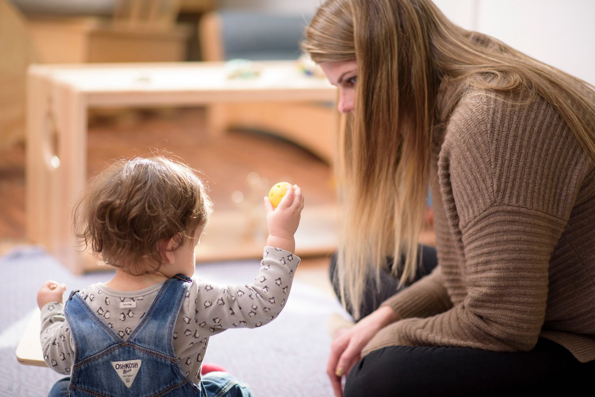 Adult kneeling beside child playing with a toy in a warm indoor room