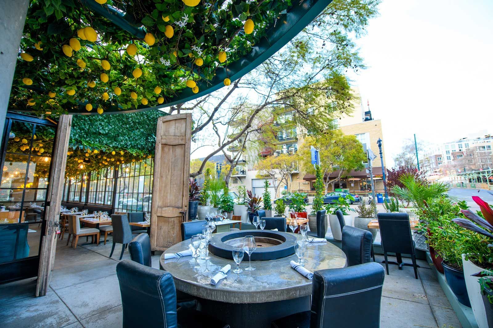 A restaurant patio with a table and chairs under a canopy of lemons.