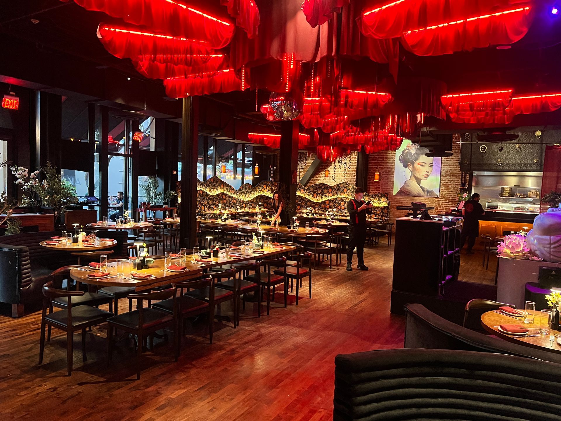 A restaurant with a lot of tables and chairs and a red sign in the middle of the room.