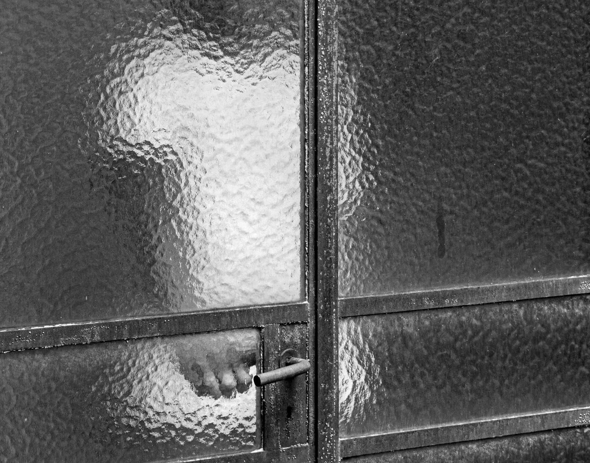 A black and white photo of a person behind a textured glass door
