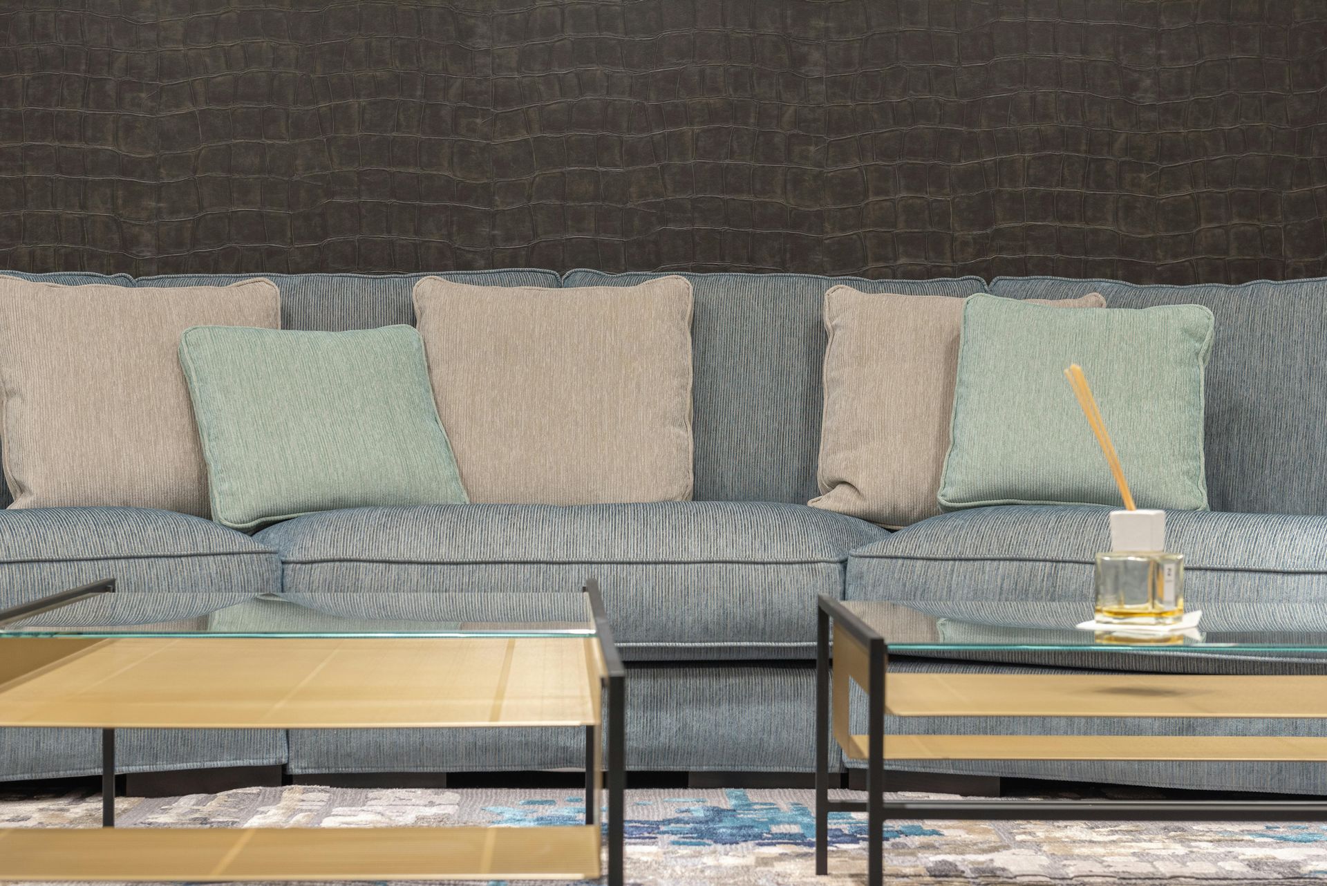 A living room with a blue couch , two glass coffee tables , and a brick wall.