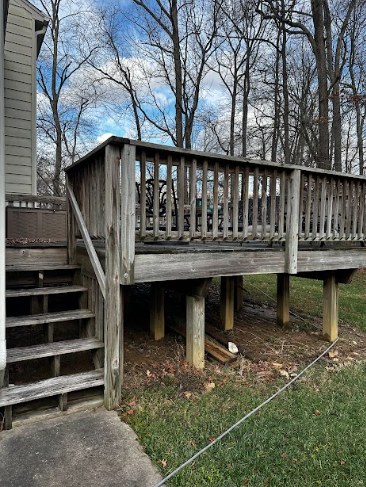 A wooden deck with stairs leading up to it is in the backyard of a house.