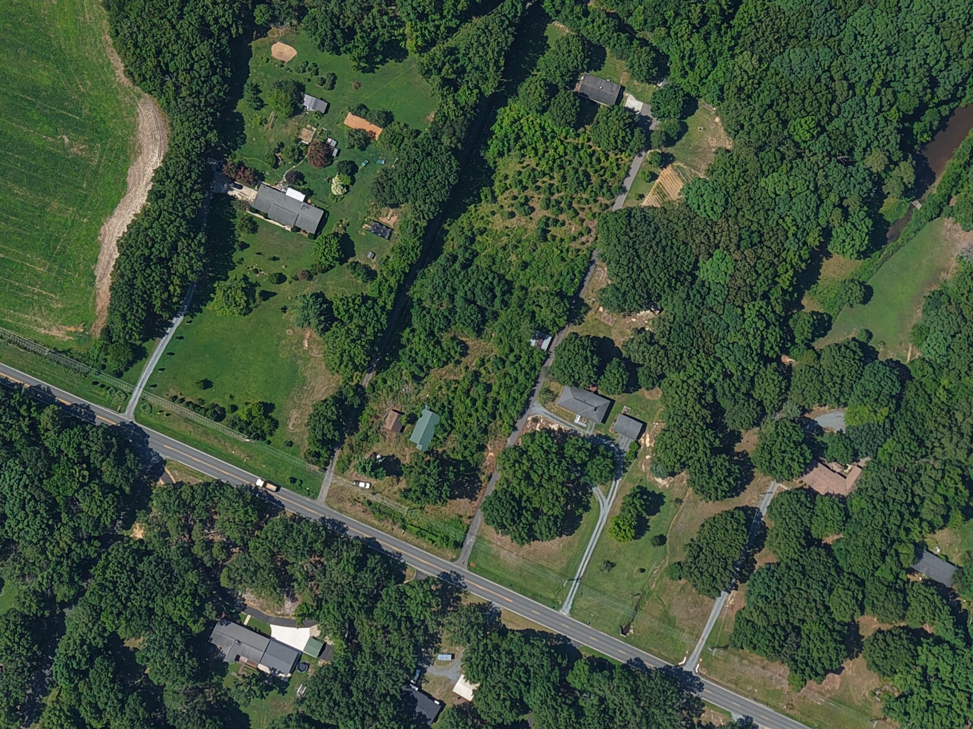 Aerial view of a rural neighborhood with scattered houses, trees, and roads beside a field.