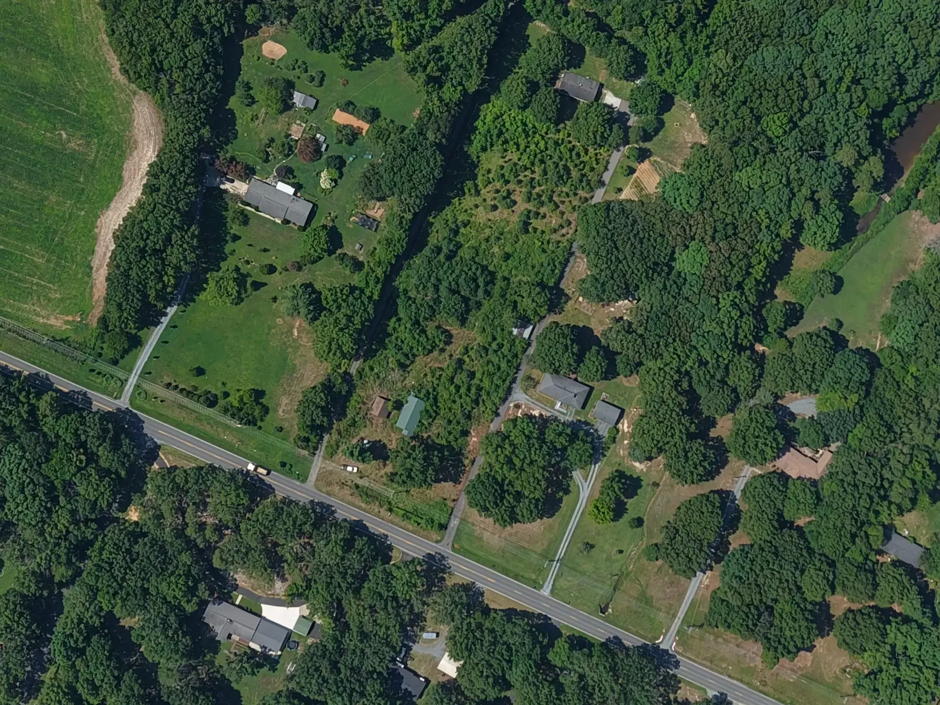 Aerial view of rural homes along a road, surrounded by dense green trees and lawns.