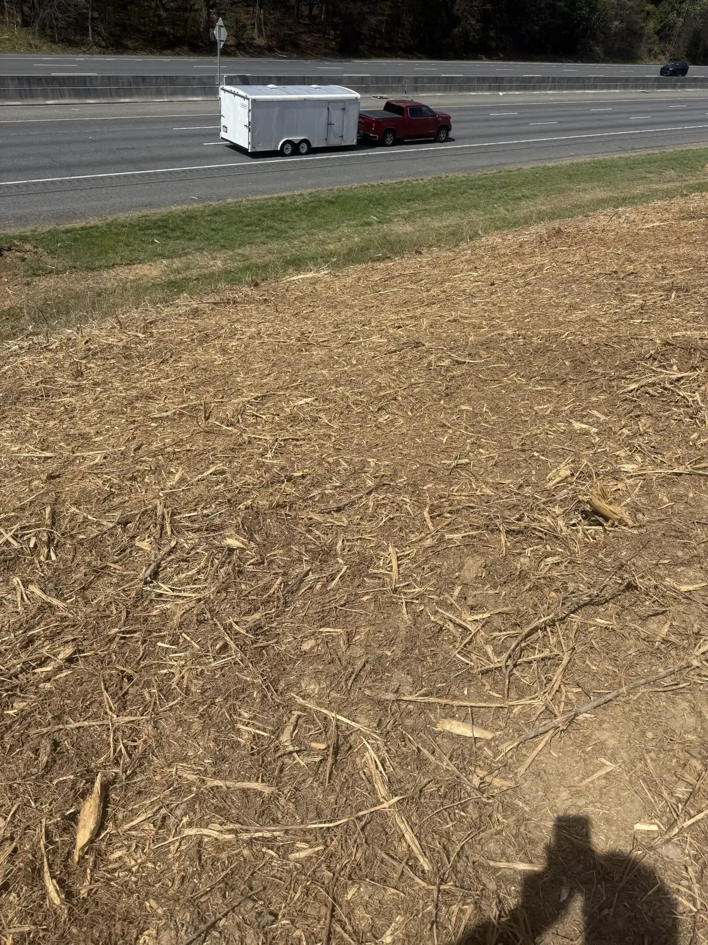 White trailer hitched to a maroon pickup on a roadside beside a grassy field and dirt foreground