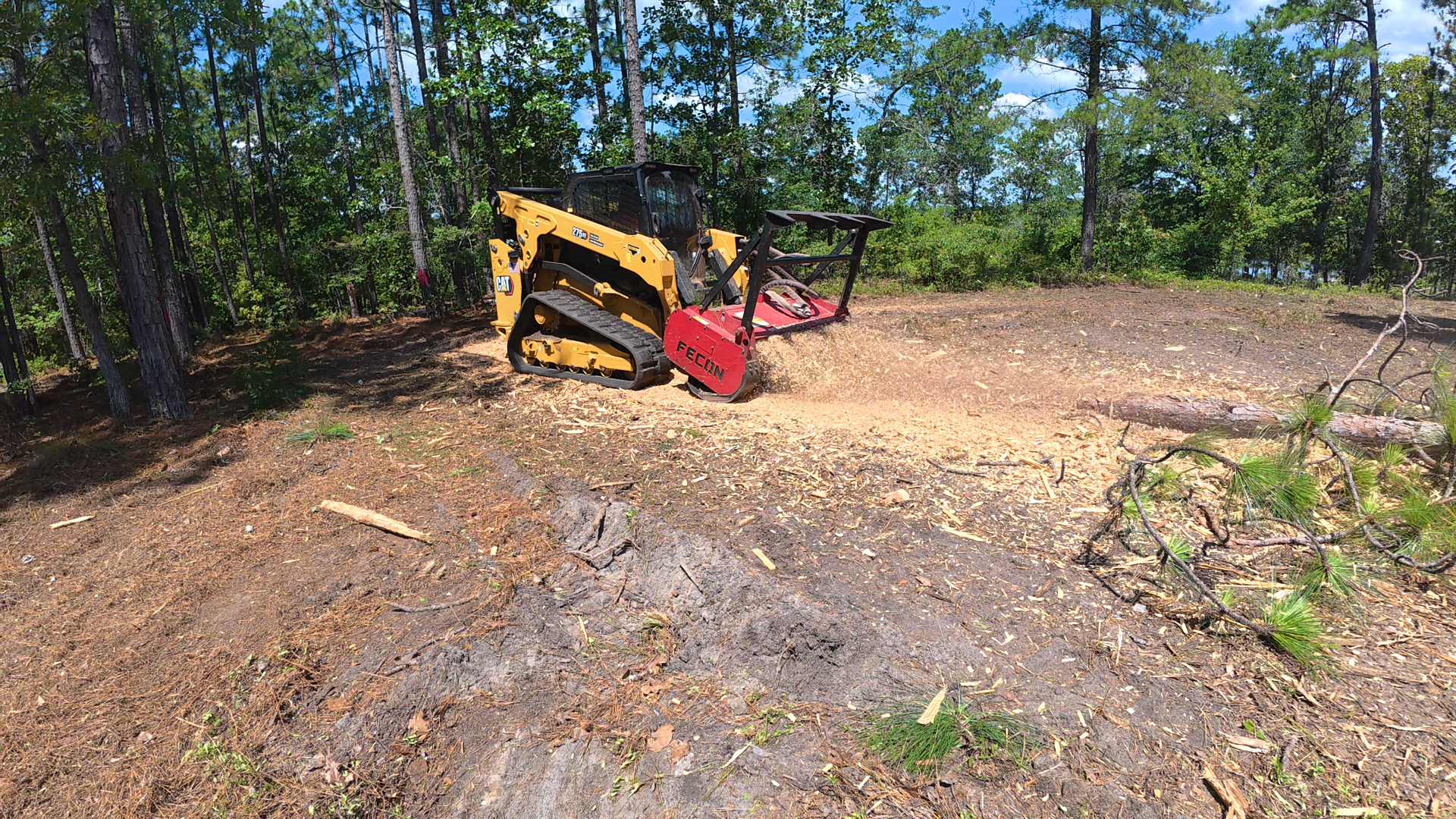 Yellow-and-red skid steer on a dirt clearing surrounded by trees