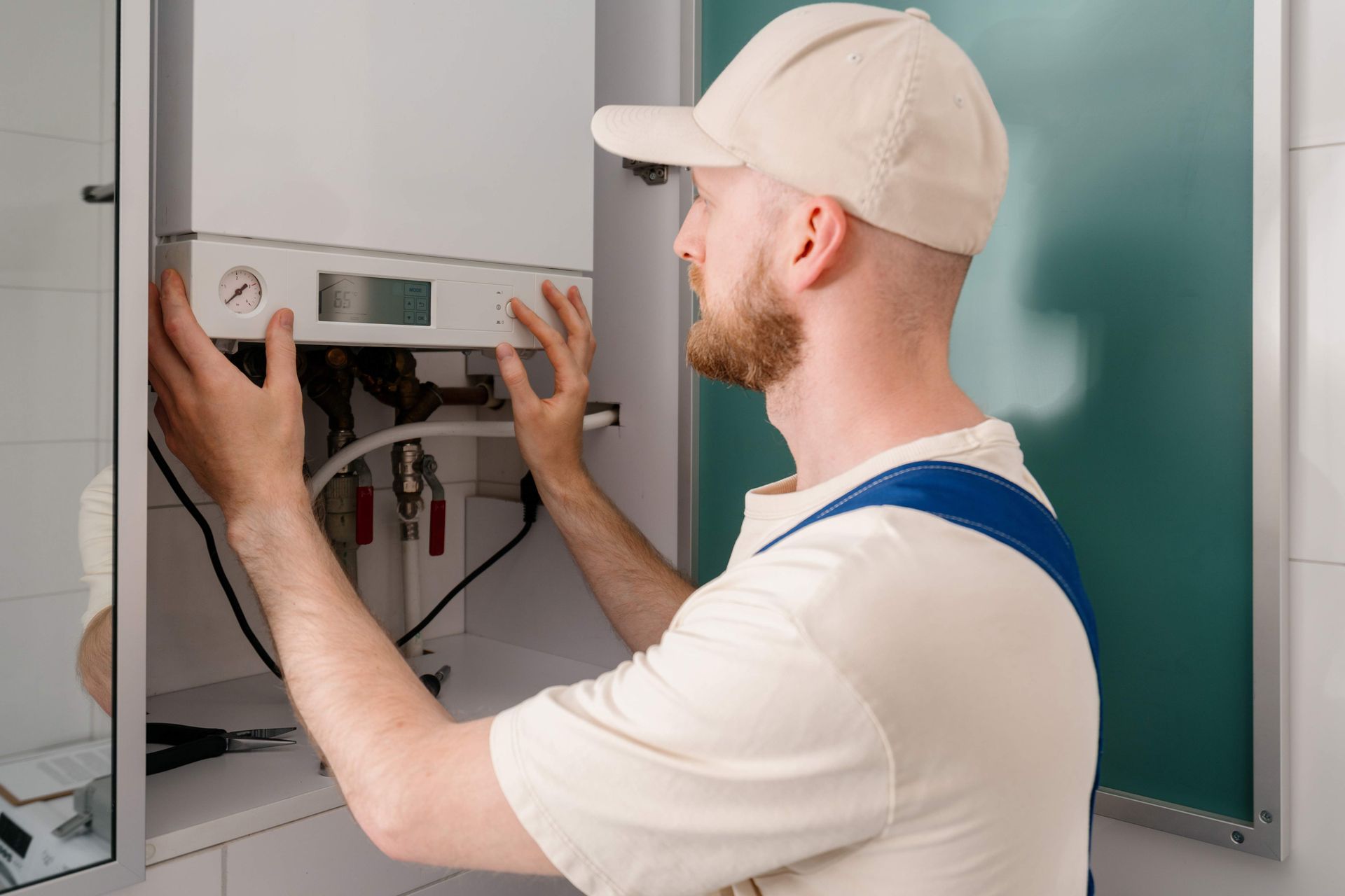 Man in work clothes fixing a white boiler mounted on a wall. Man in work clothes fixing a white boiler mounted on a wall.