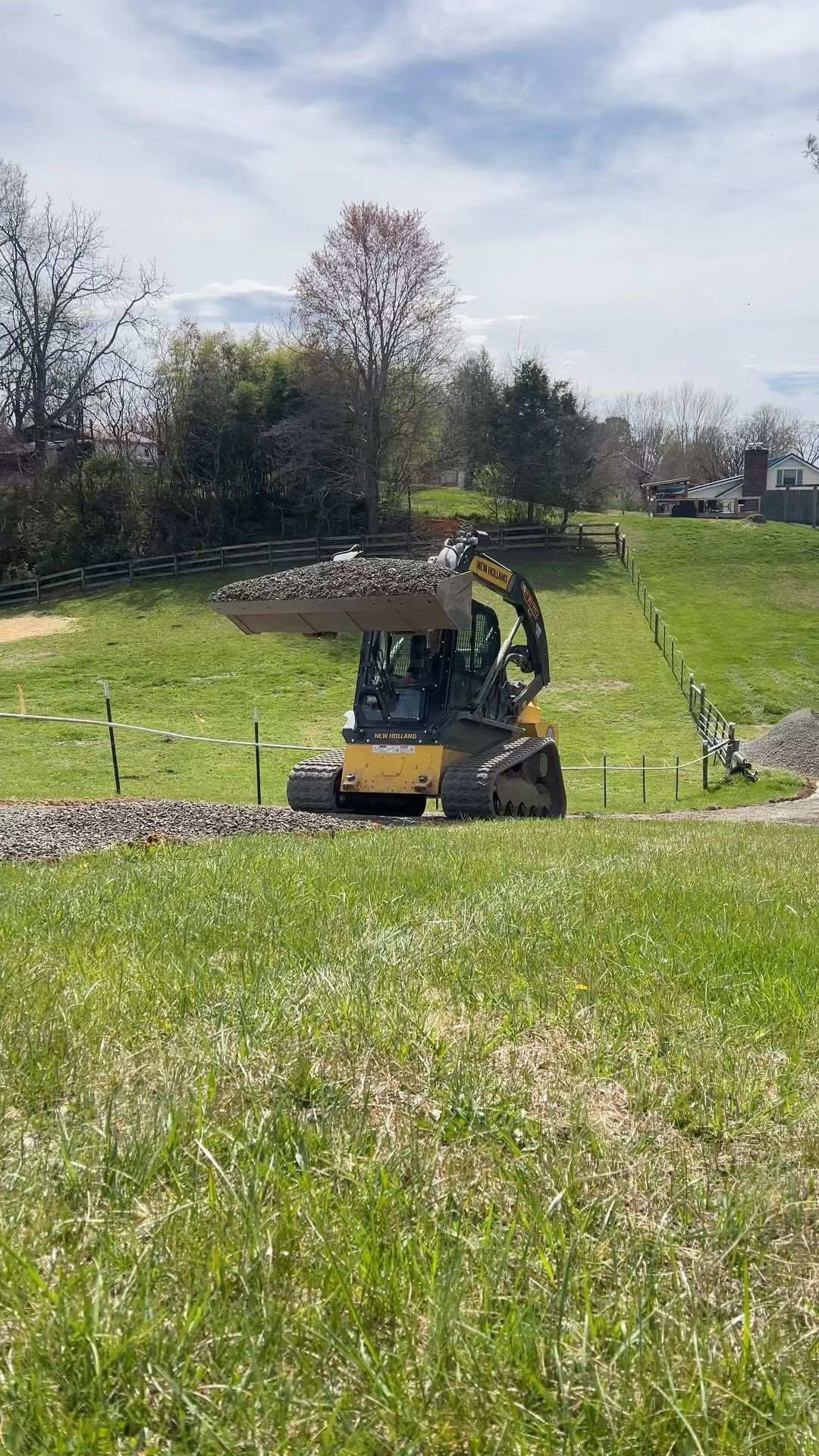 Yellow excavator, bucket full of rocks, operating on a grassy hillside.