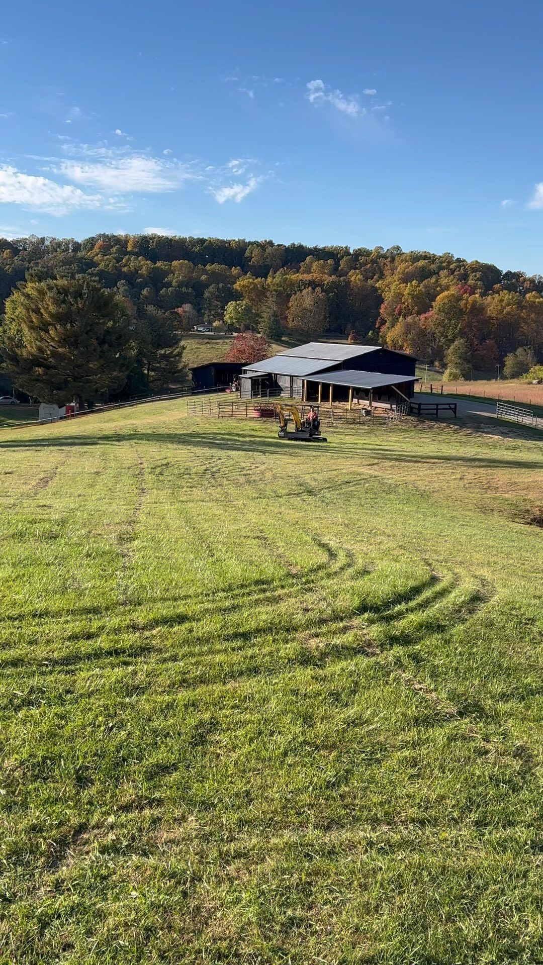 Grassy field slopes toward a barn and fall trees under a blue sky.