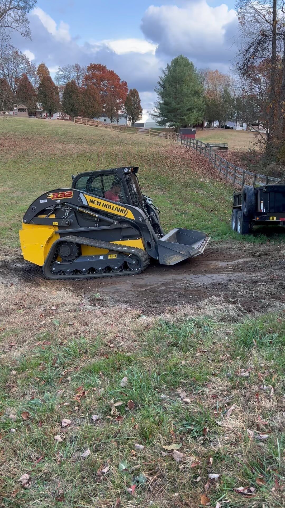Yellow and black skid steer loader on a grassy hill, with a trailer in the background.