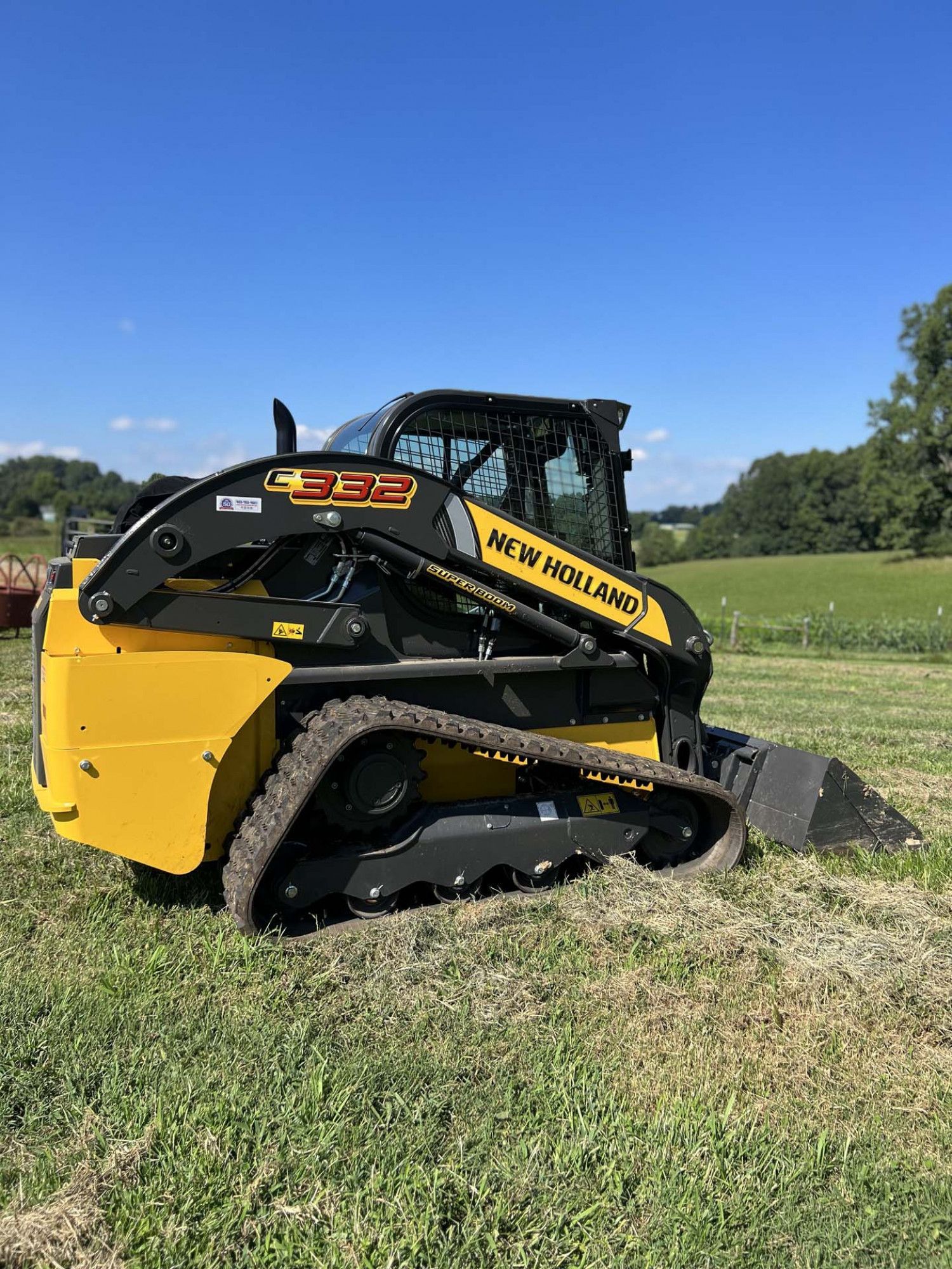 Yellow and black New Holland C332 compact track loader on grass.