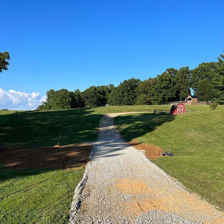 Gravel pathway through a grassy park, leading towards trees and a bright blue sky.