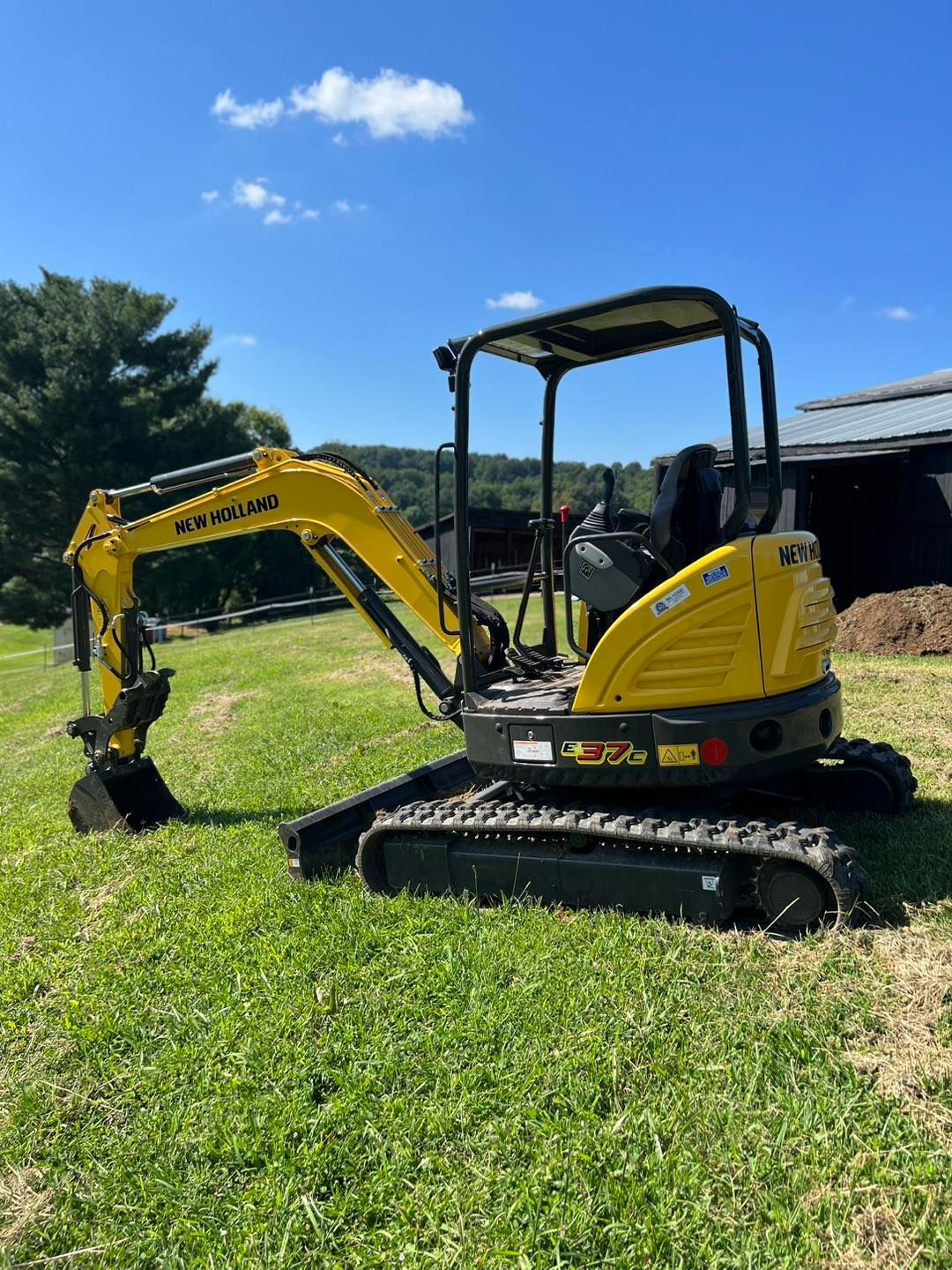 Yellow excavator on grass with blue sky in background.
