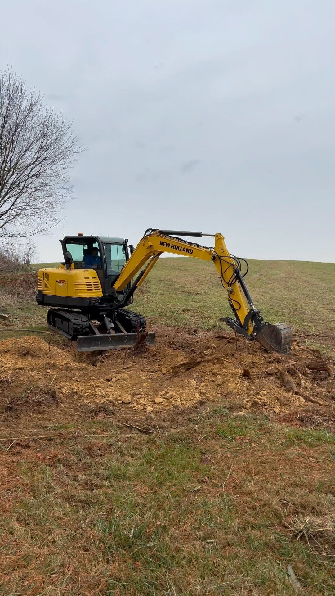 Yellow excavator digging in a field under a cloudy sky.