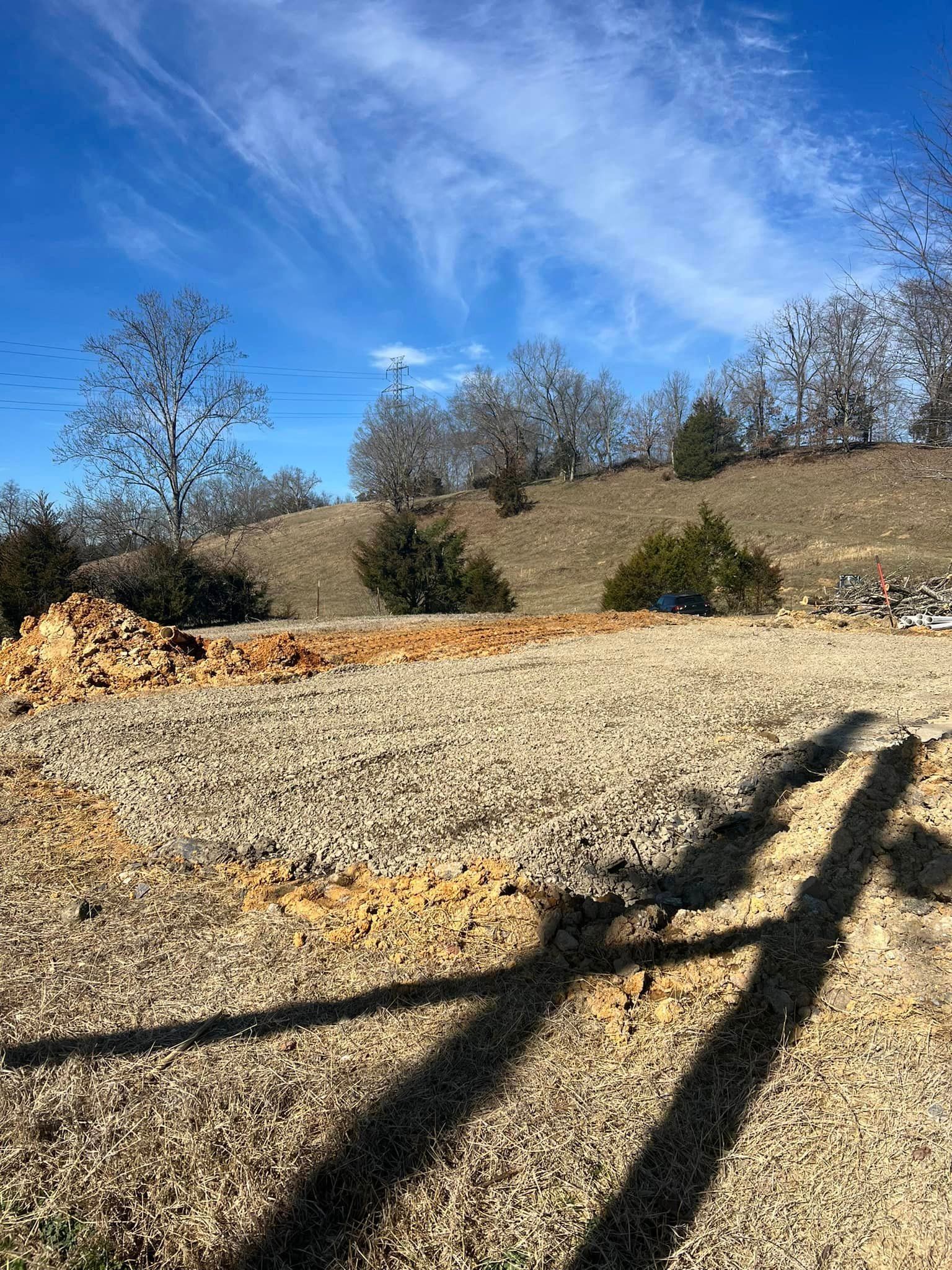 Field of dry grass and dirt, with trees on a small hill under a blue sky with streaky clouds.