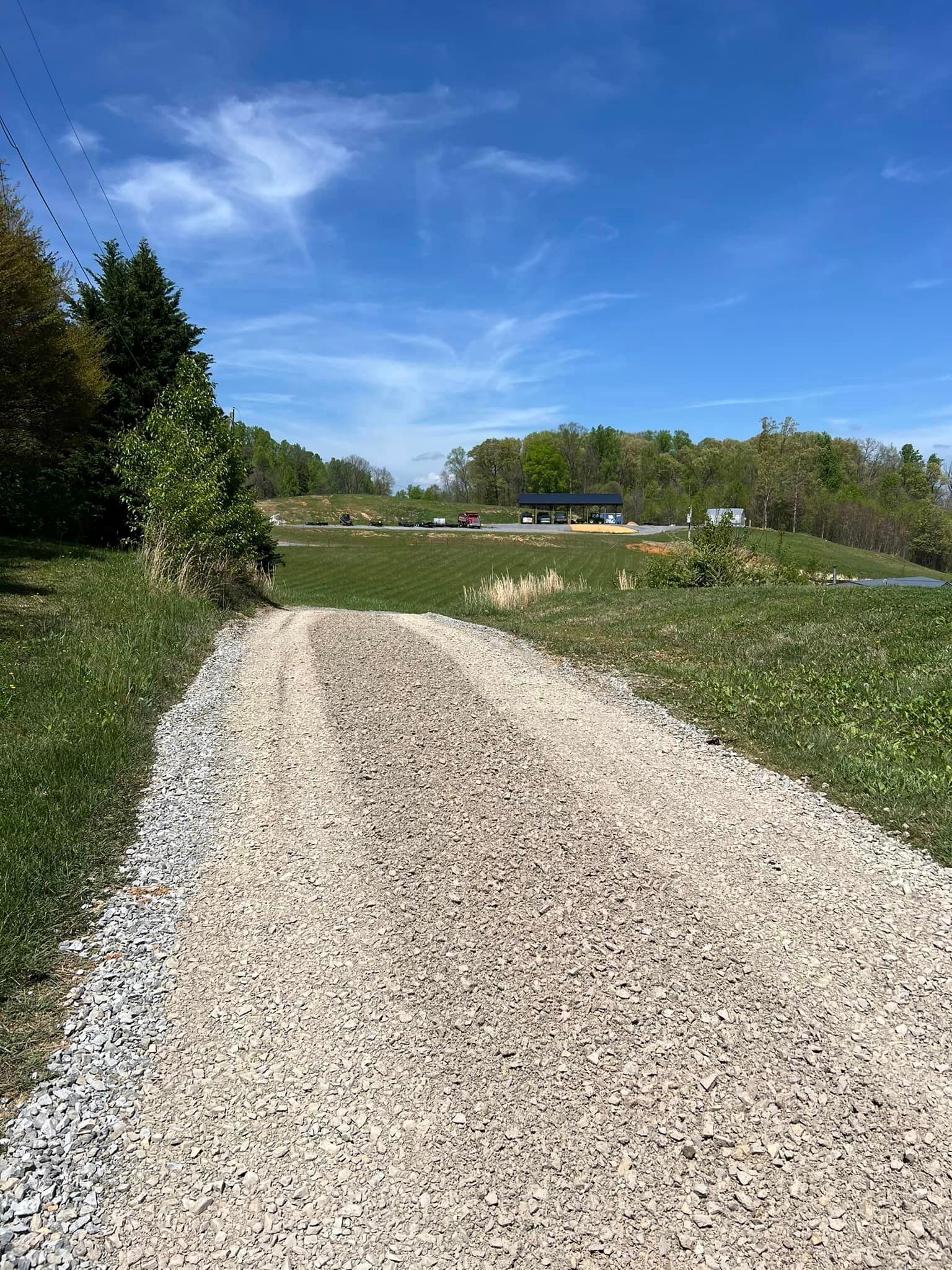 Gravel path leading uphill toward a pavilion under a blue sky, surrounded by greenery.