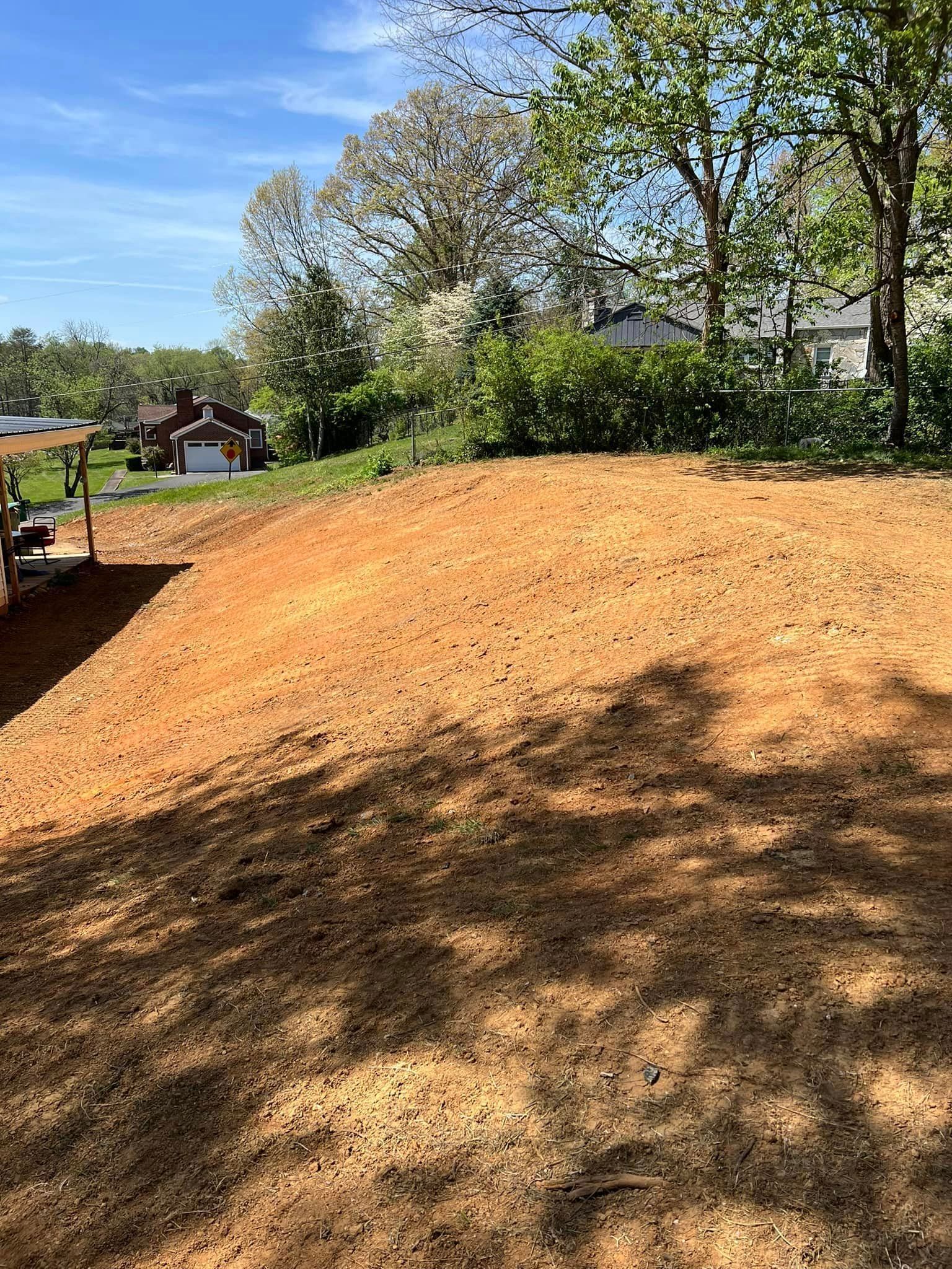 Newly seeded yard, brown soil, under blue sky, with trees in the background.