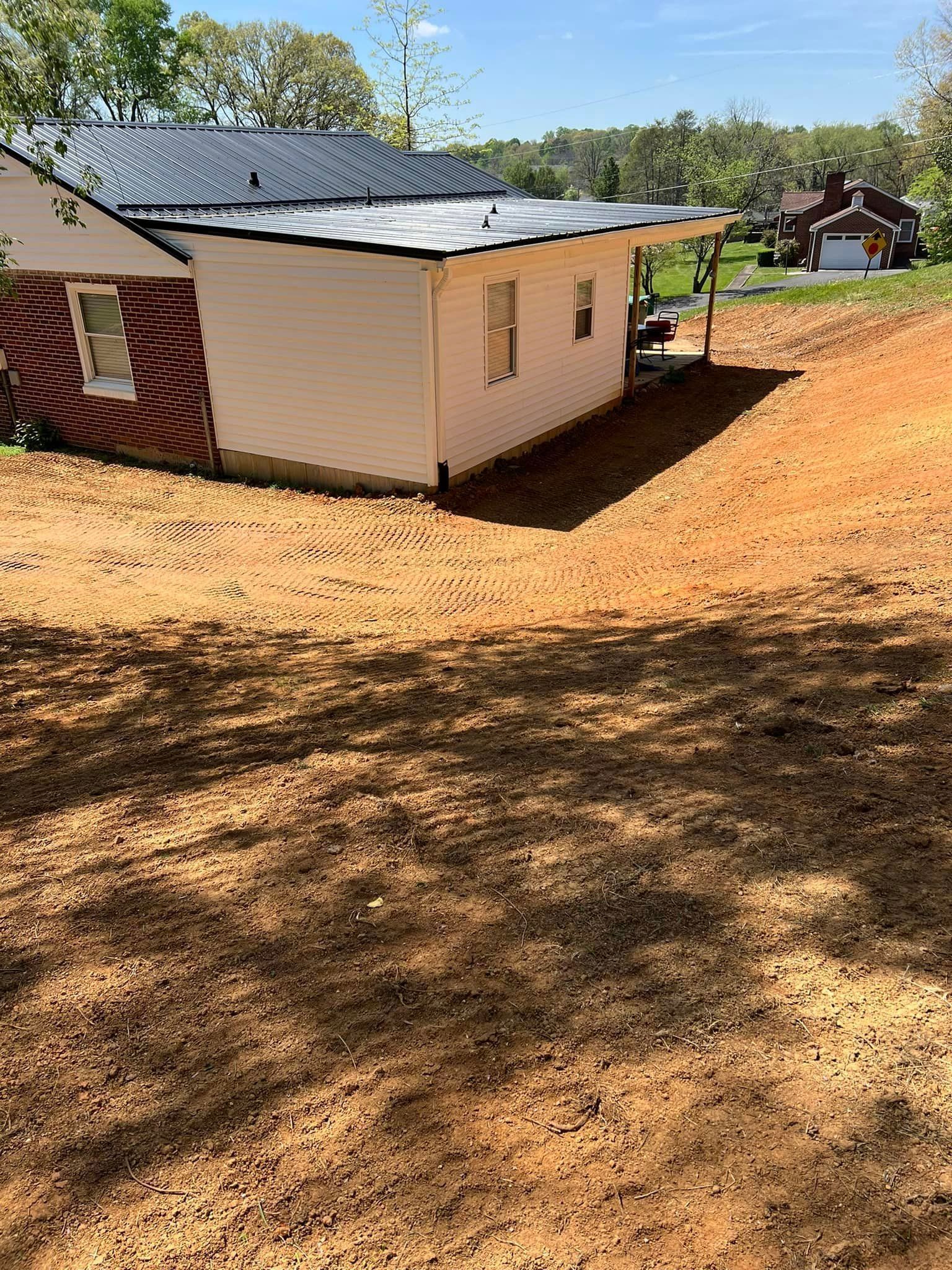 Building with white siding and black roof on freshly graded brown soil.