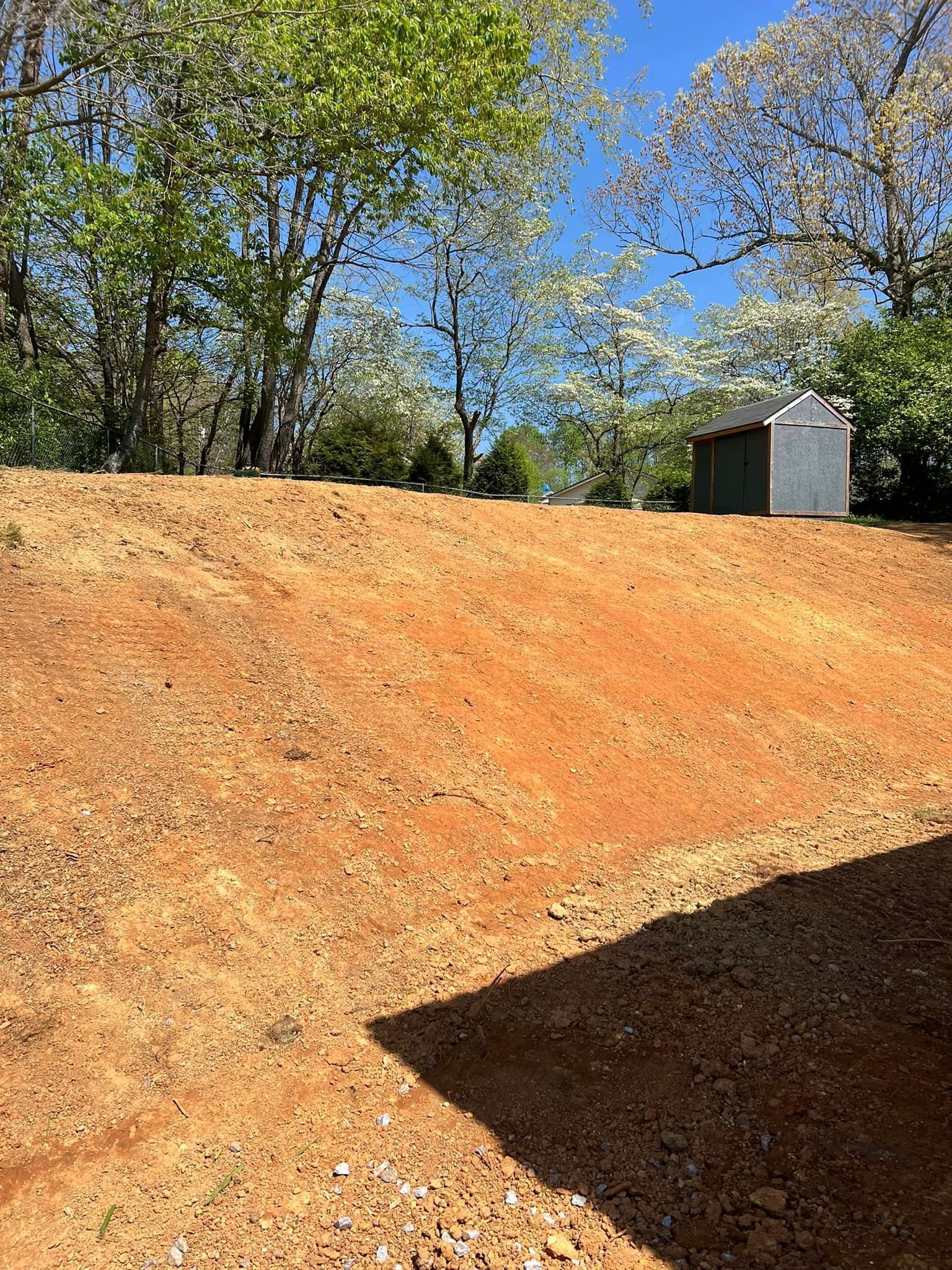 Dirt clearing with shed in the background, trees, and blue sky.