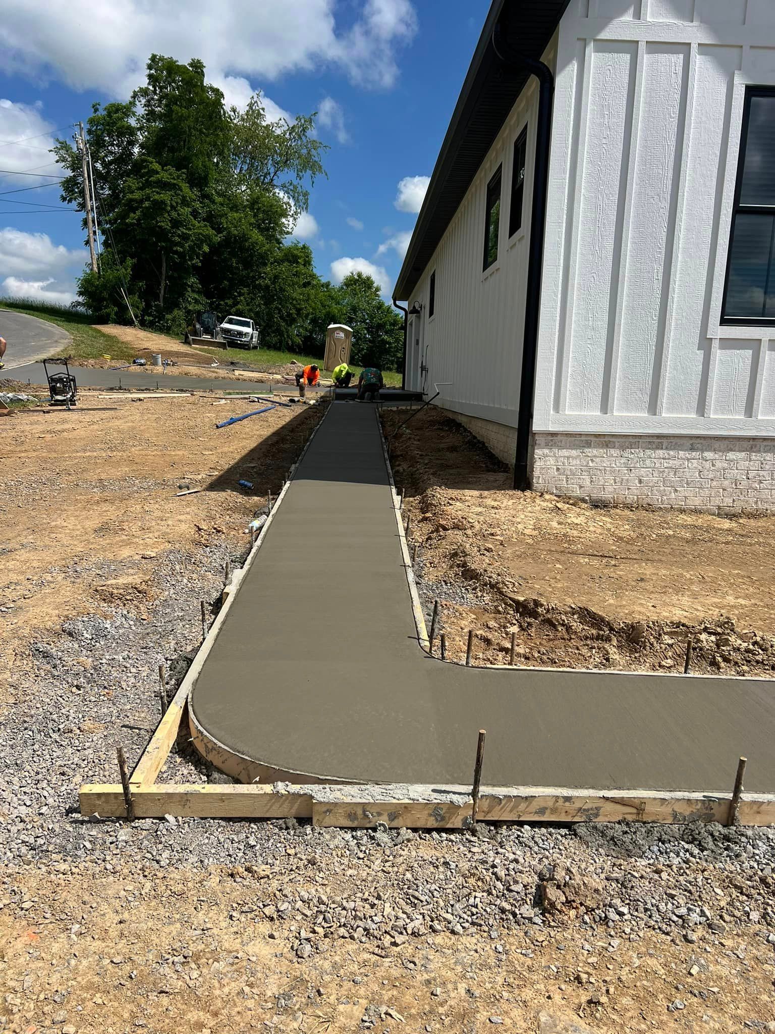 New concrete sidewalk alongside a white house under construction on a sunny day.