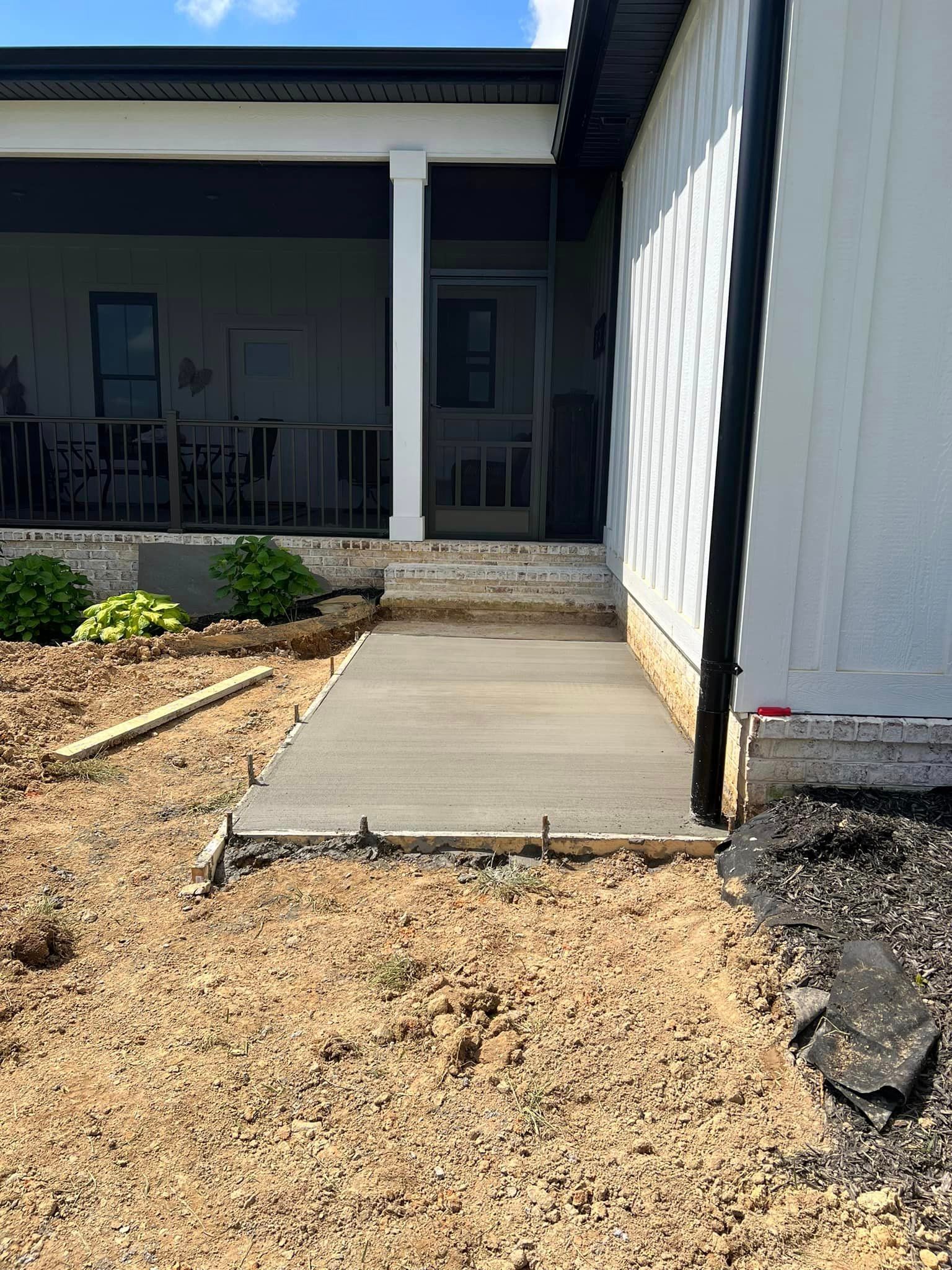 Newly poured concrete walkway leading to a house porch. Construction materials surround it.