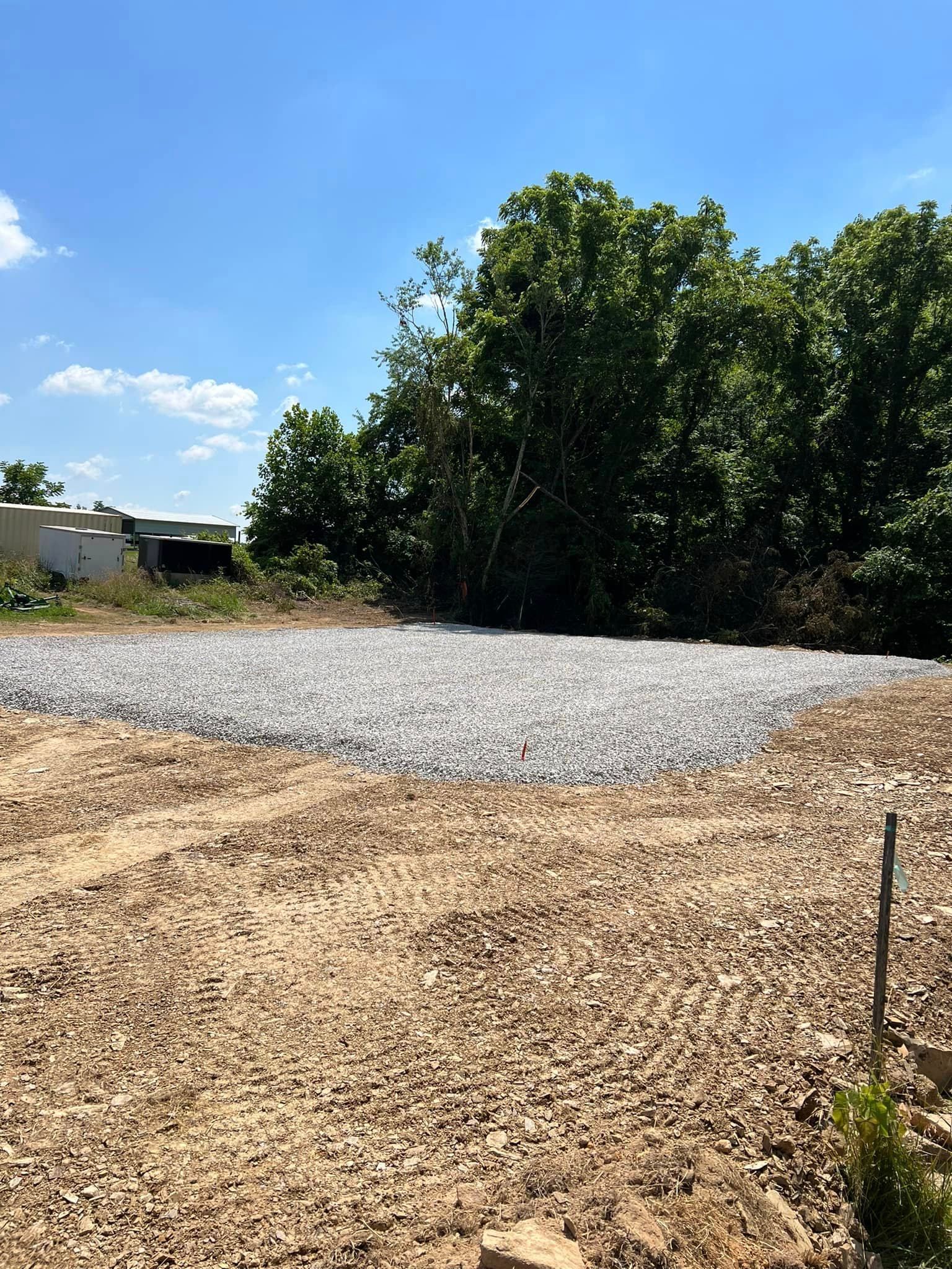 Gravel bed on a dirt lot, trees in the background, blue sky.