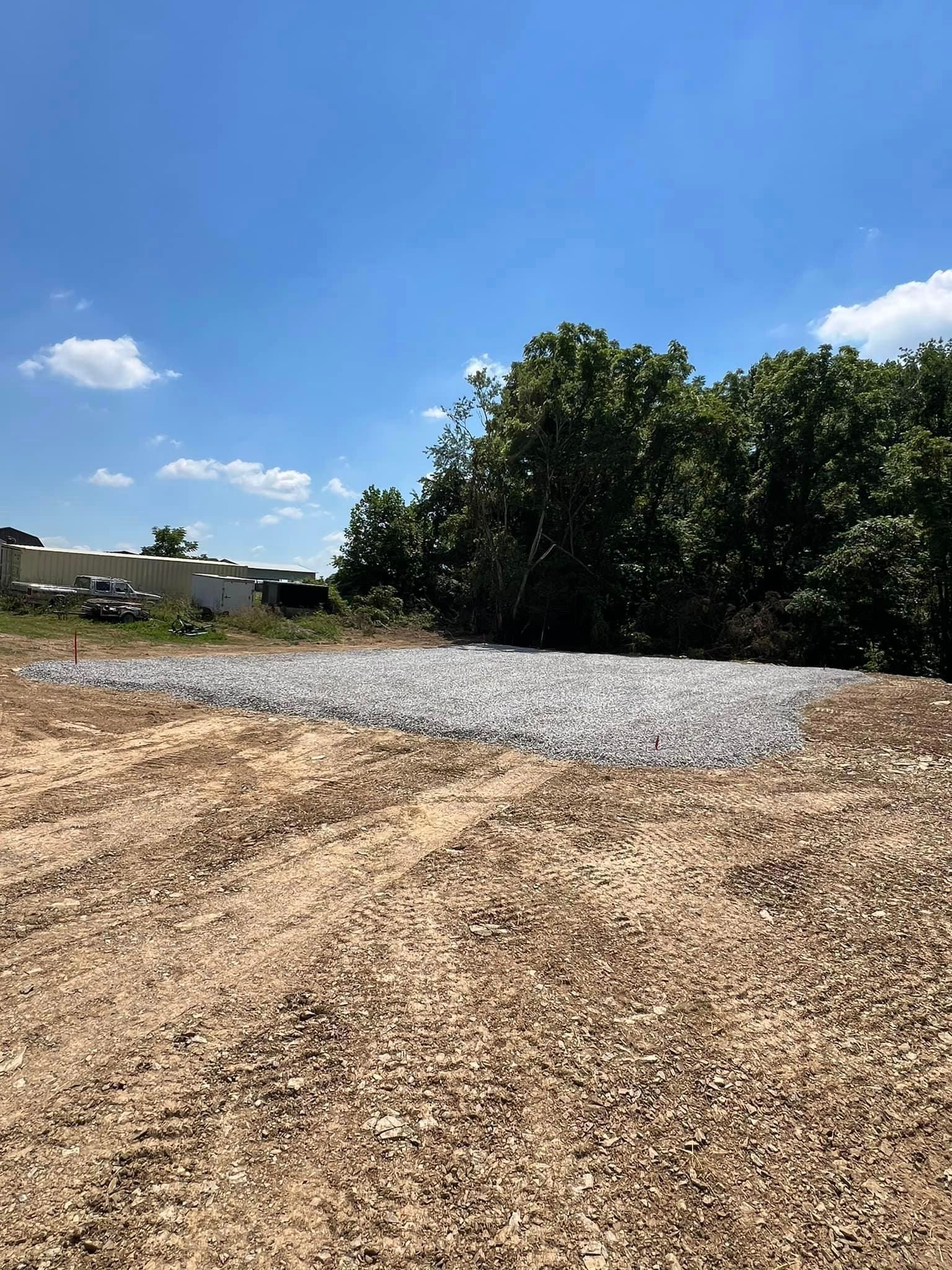 A gravel-covered plot of land next to a wooded area under a blue sky.